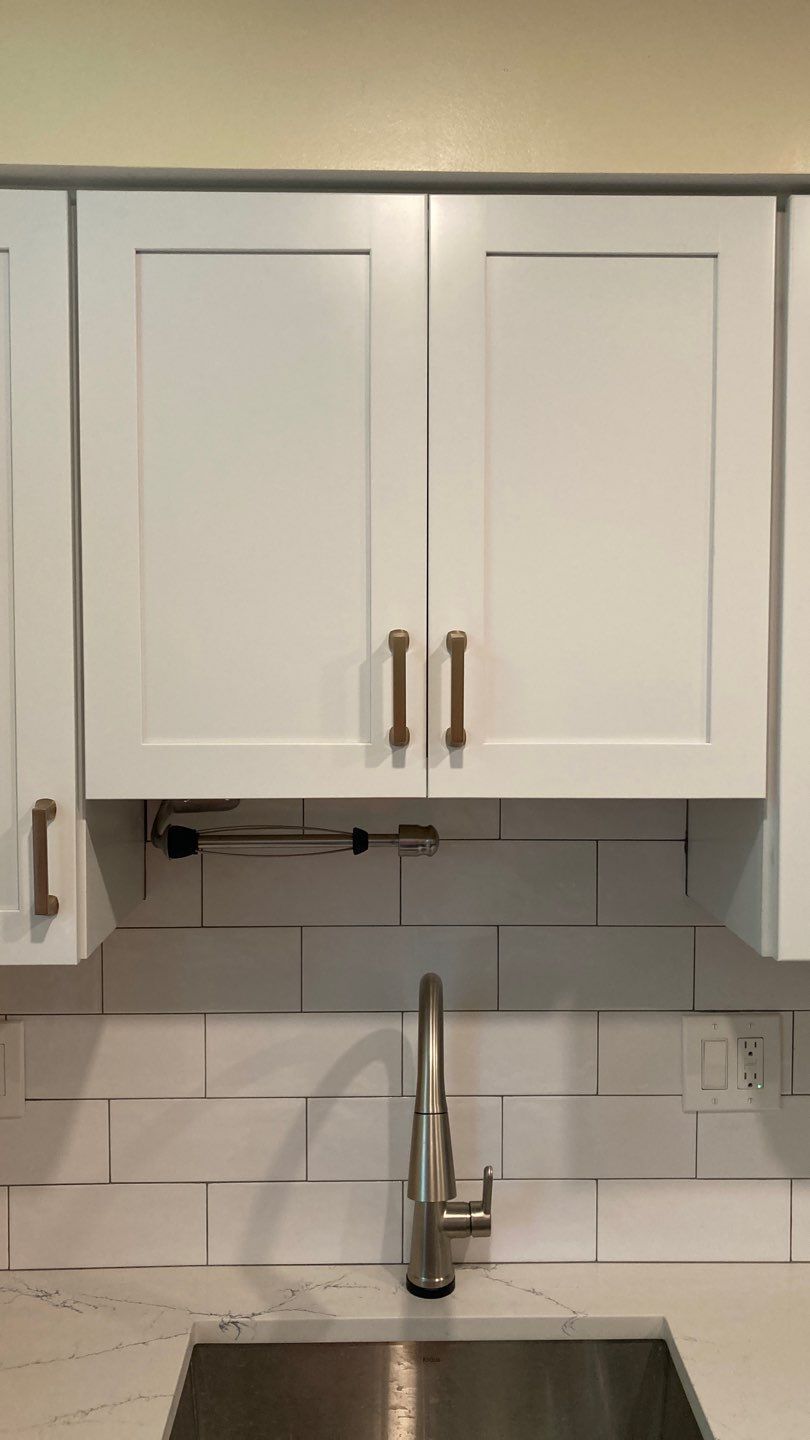 White kitchen cabinets with gold hardware above a sink with a stainless steel faucet.