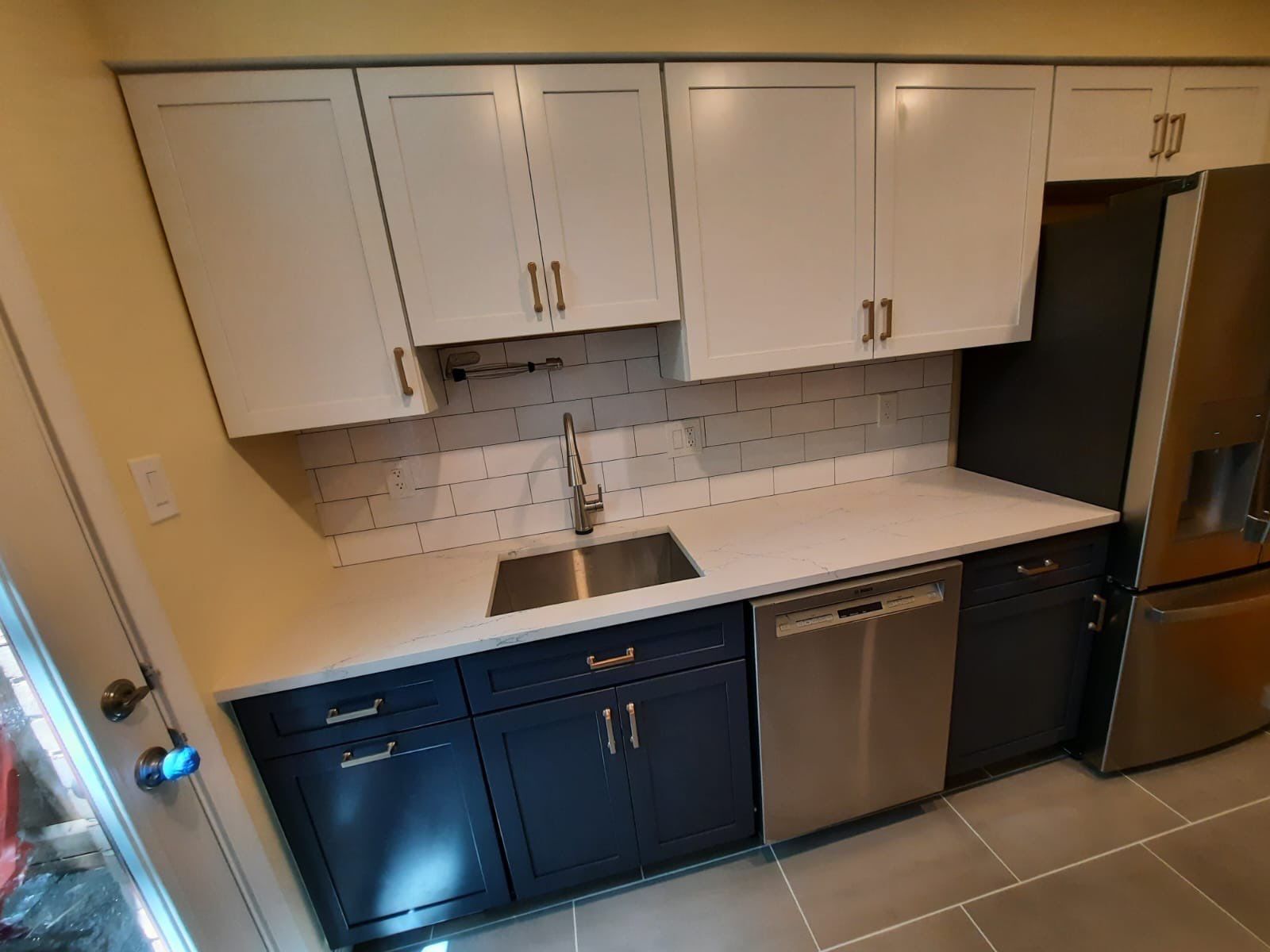 Modern kitchen with white upper cabinets, navy blue lower cabinets, stainless steel appliances, and a white countertop.