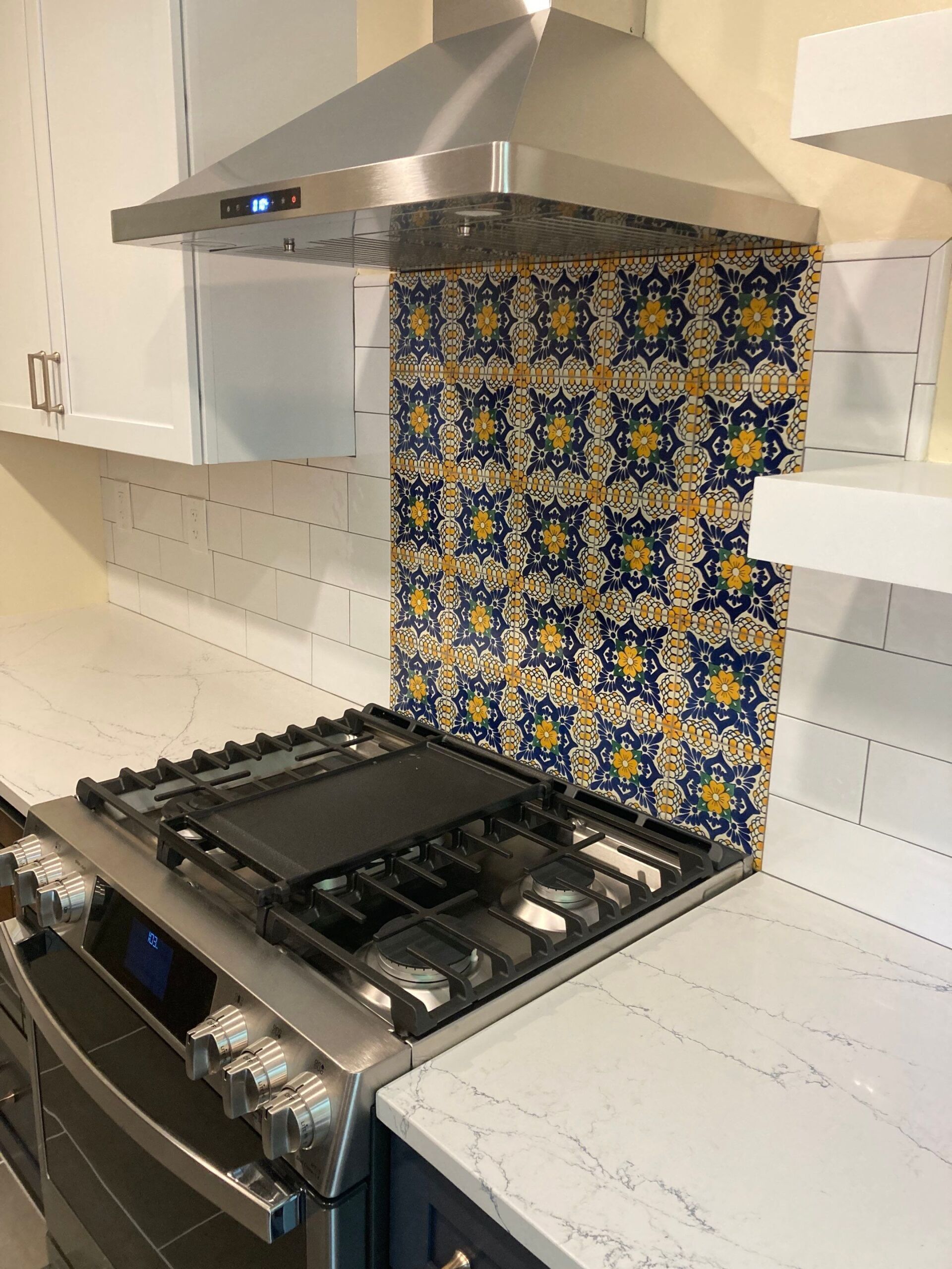 Kitchen with stainless steel stove, hood, and backsplash of patterned blue and yellow tiles.