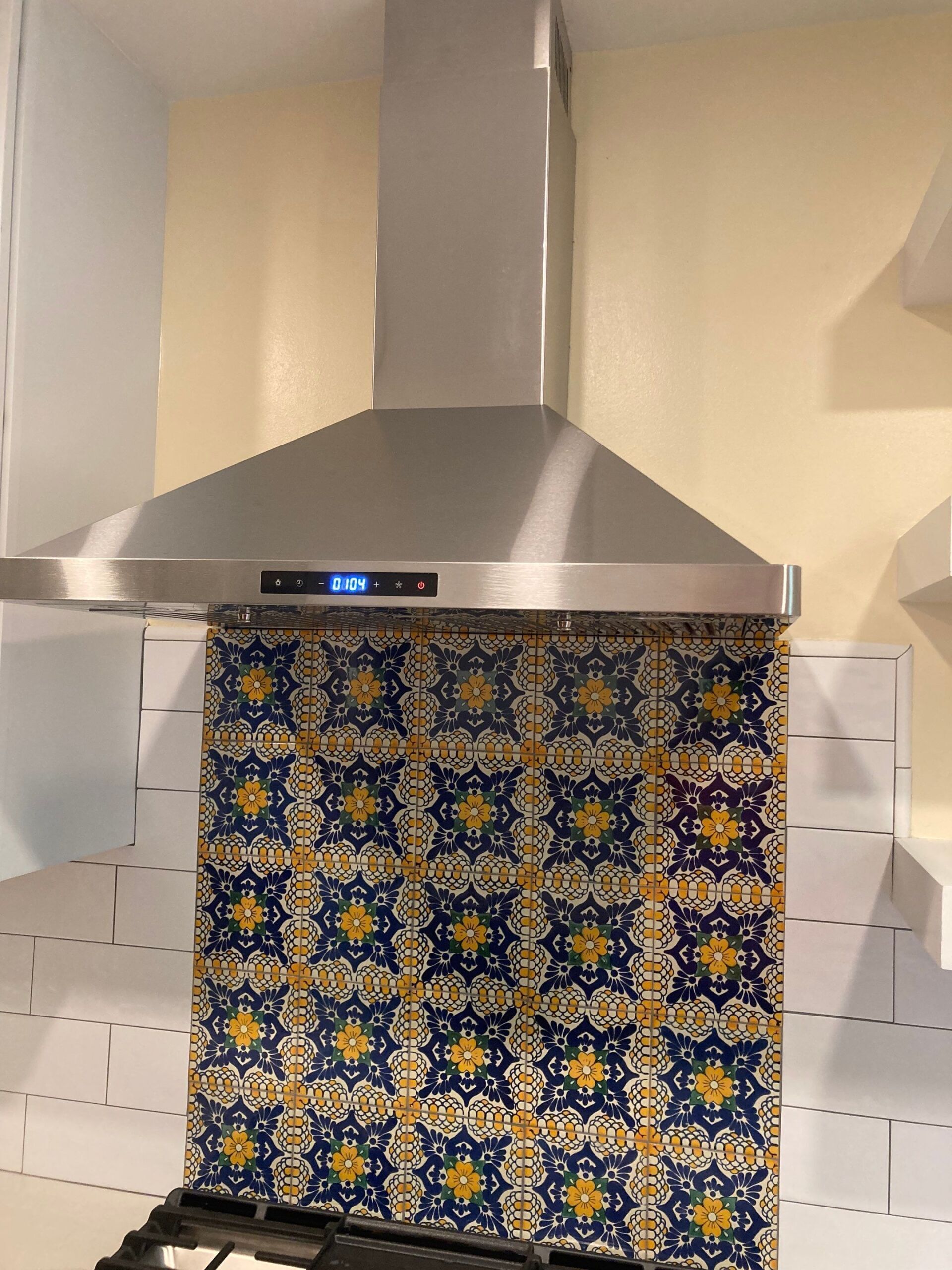 Stainless steel range hood above a stovetop with blue and yellow patterned backsplash.