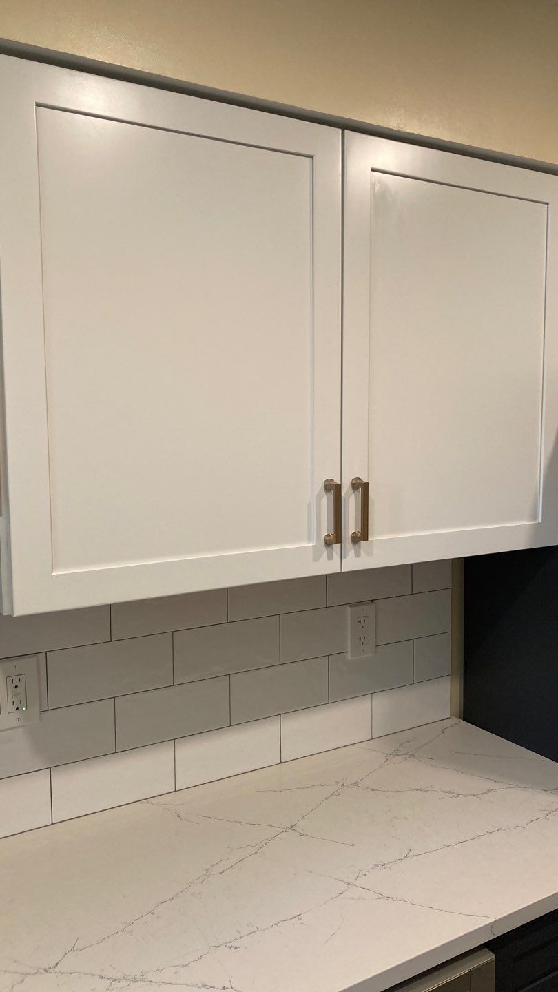 White kitchen cabinets with gold hardware above a countertop and subway tile backsplash.