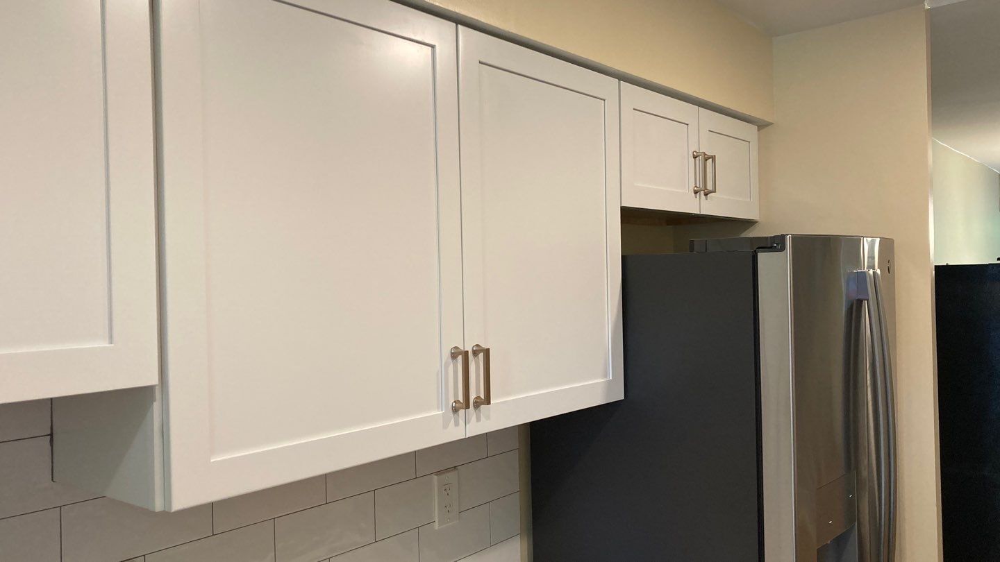 White kitchen cabinets with gold hardware above a stainless steel refrigerator.