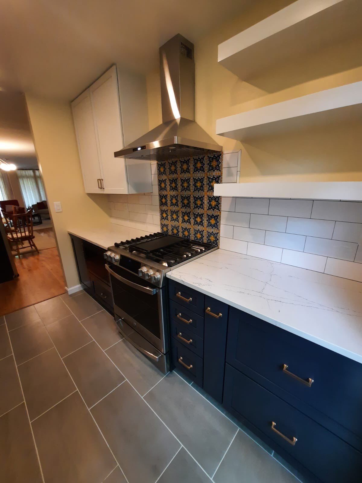 Modern kitchen: Stainless steel range, navy cabinets, patterned backsplash, white countertops, and floating shelves.