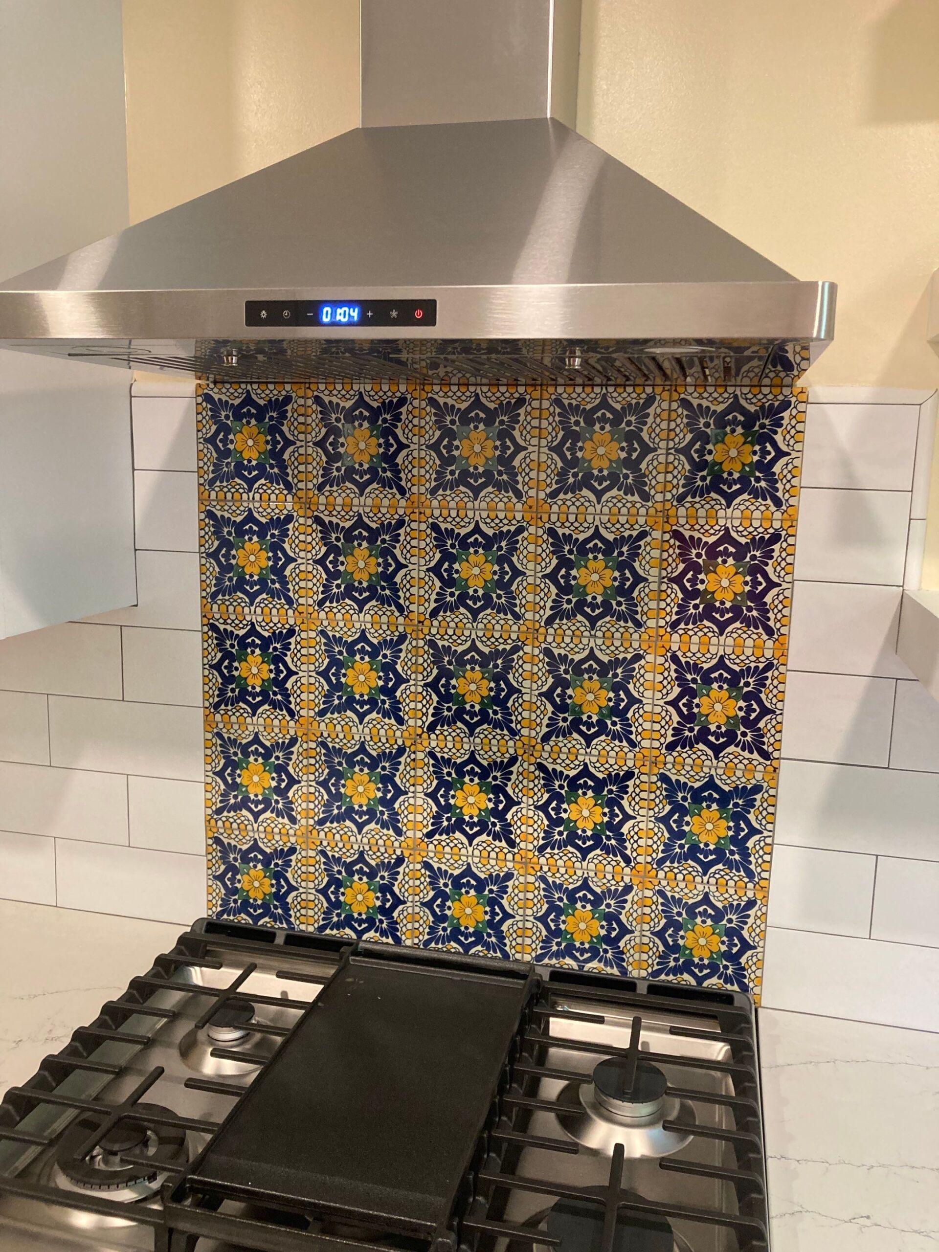 Kitchen with stove and range hood, featuring patterned blue and yellow tile backsplash.