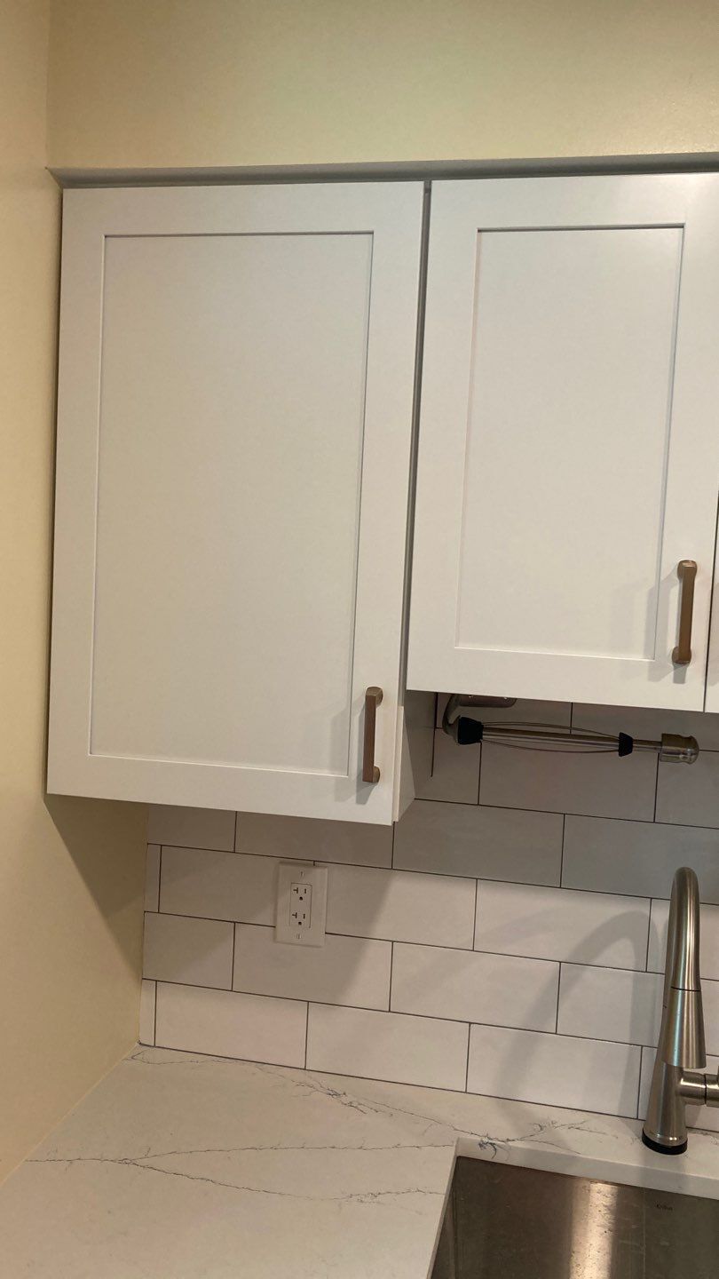 White kitchen cabinets above a white subway tile backsplash and countertop, with a stainless steel faucet.