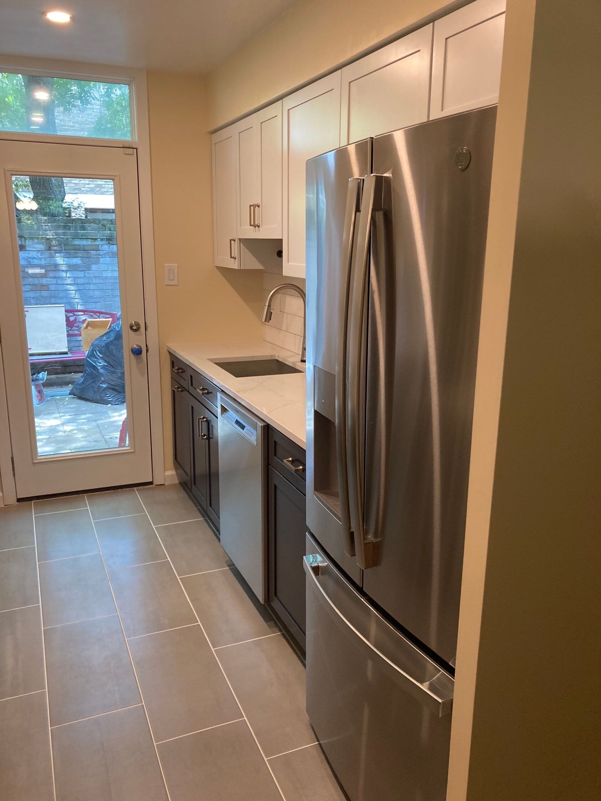 A narrow kitchen with white cabinets, stainless steel appliances, and a door to a patio.