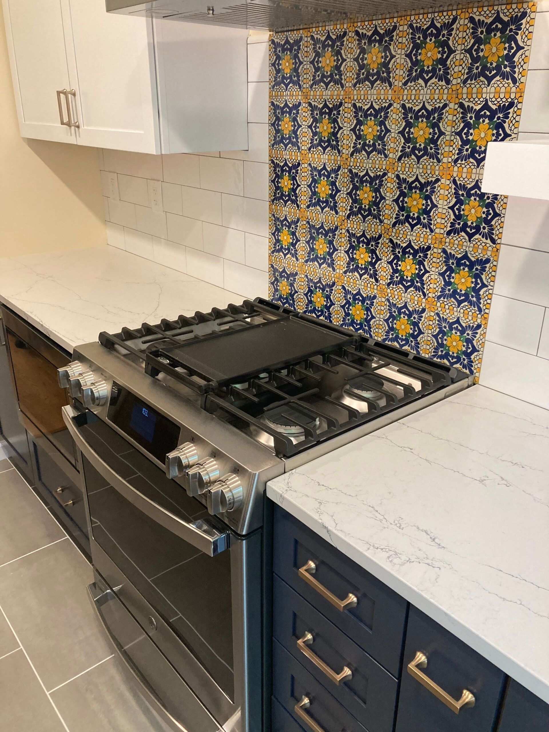 Kitchen with stainless steel range, blue and gold tile backsplash, and blue cabinets with gold handles.