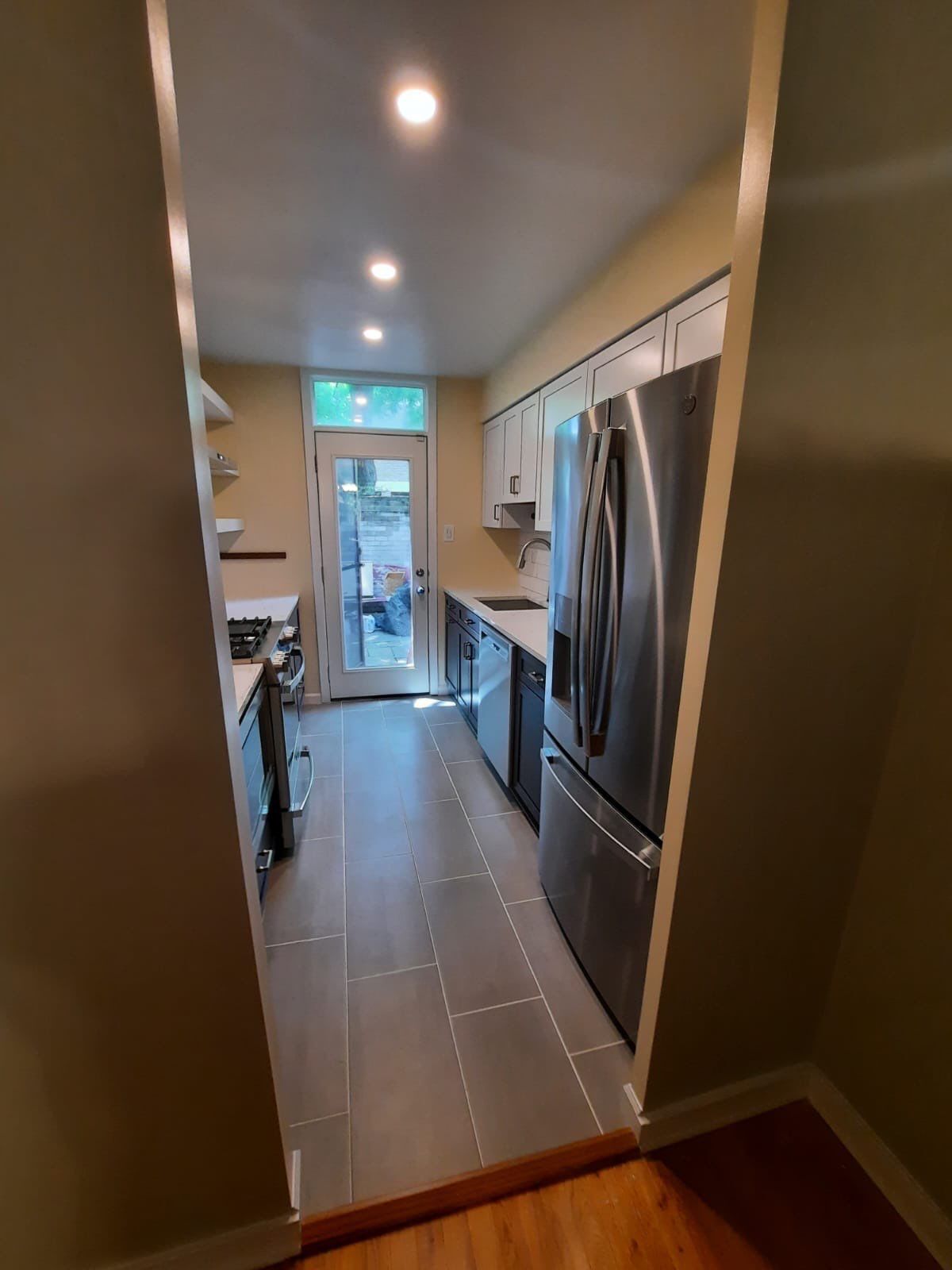 Narrow galley kitchen with stainless steel appliances, tile floor, and a door leading outside.
