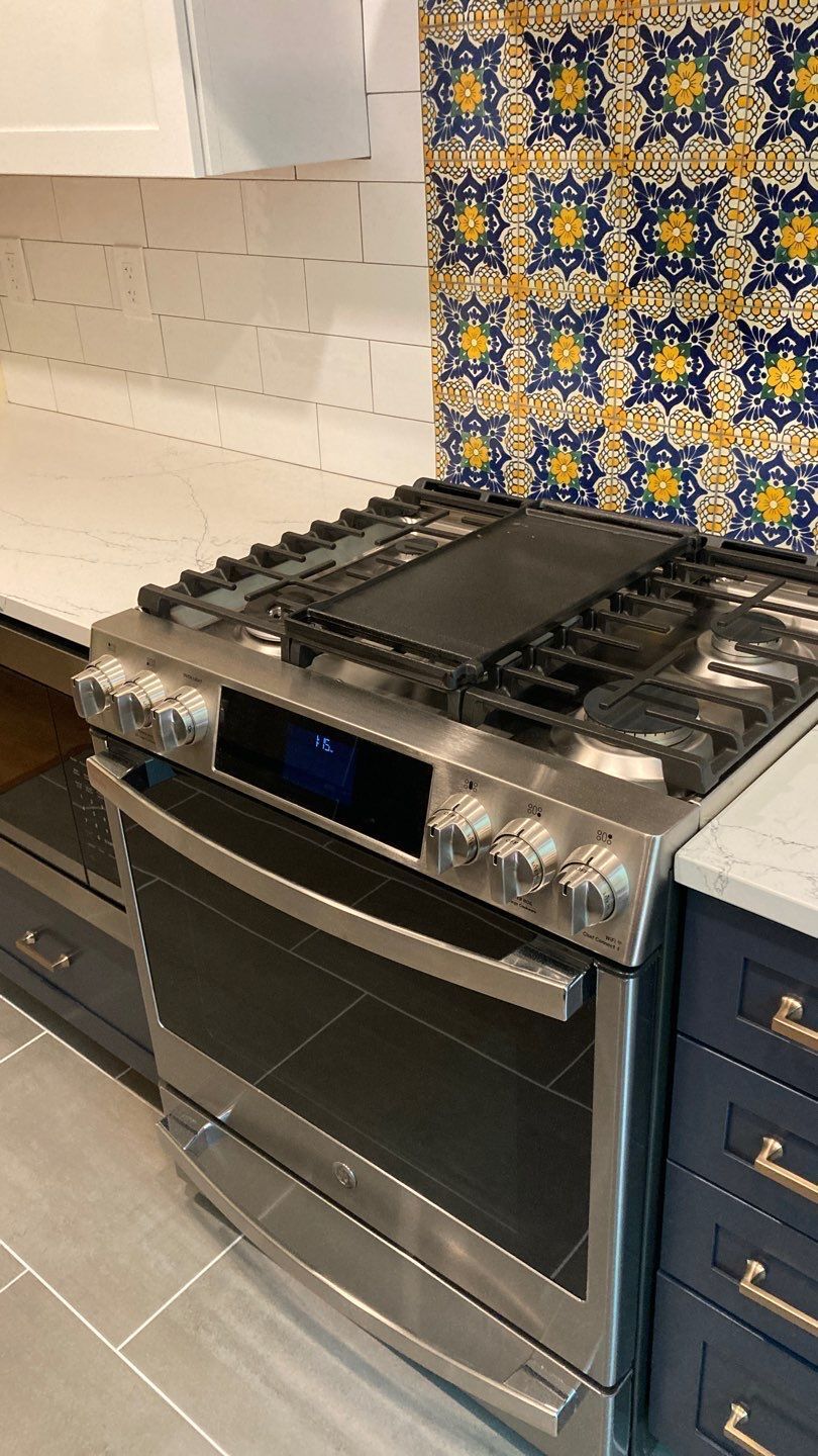 Stainless steel gas range in kitchen with blue tile backsplash.