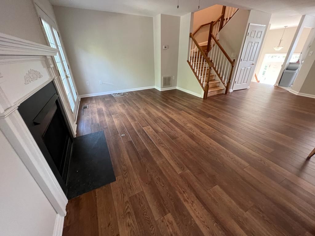 Empty living room with dark wood flooring, fireplace, and staircase.