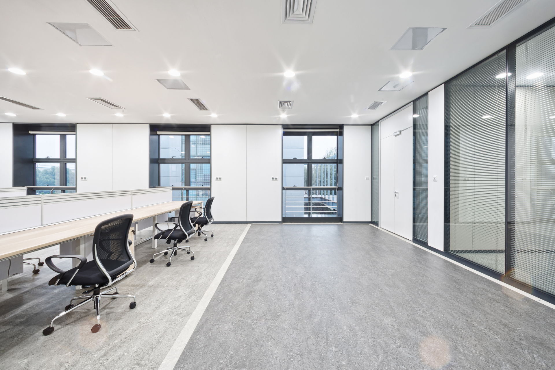 A modern, minimalist office space with white walls, black office chairs, desks, and glass-paneled meeting rooms.