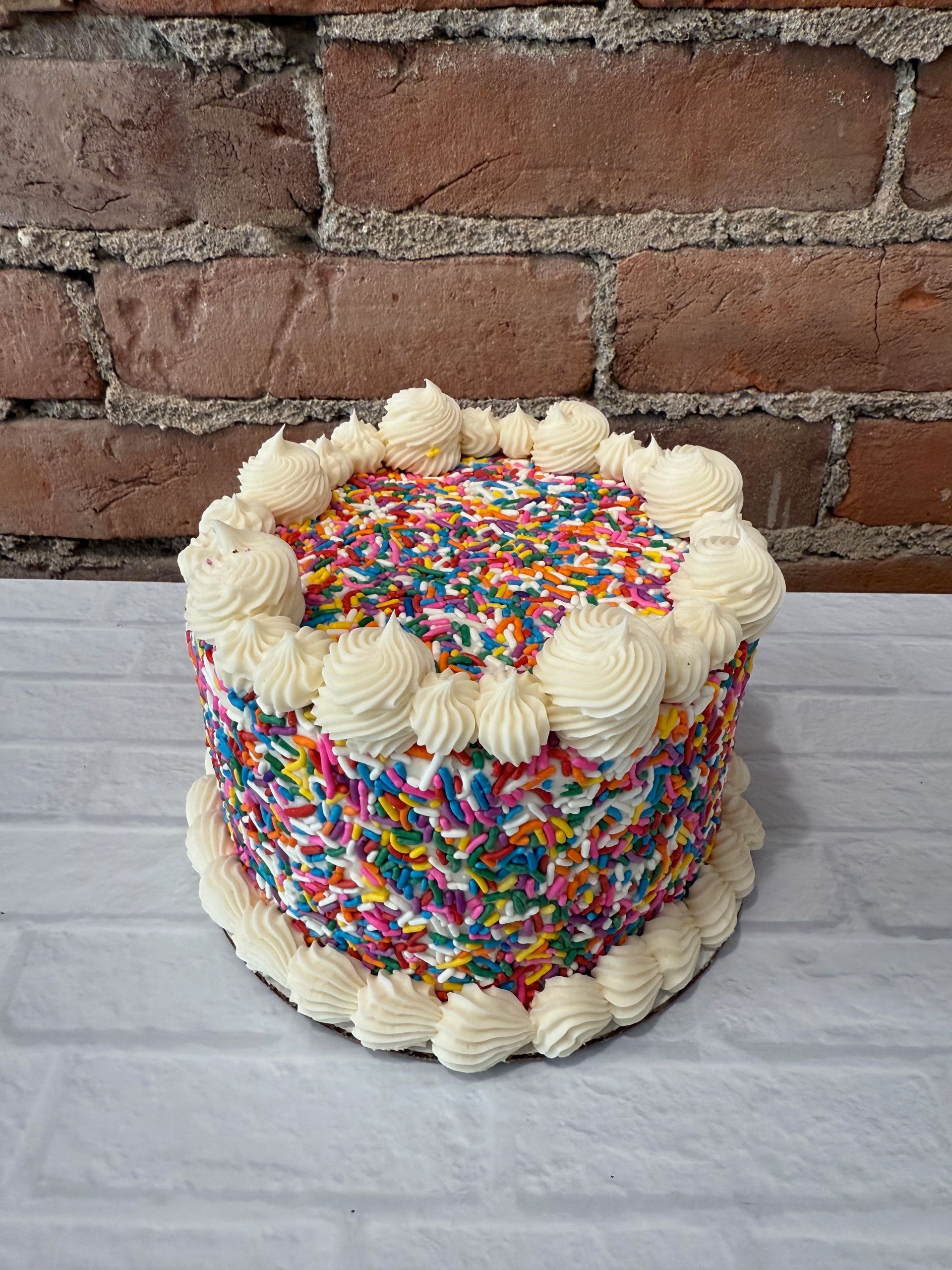 A cake with sprinkles and frosting is sitting on a table in front of a brick wall.