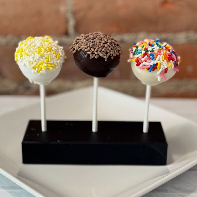 Three cake pops with different toppings on a white plate