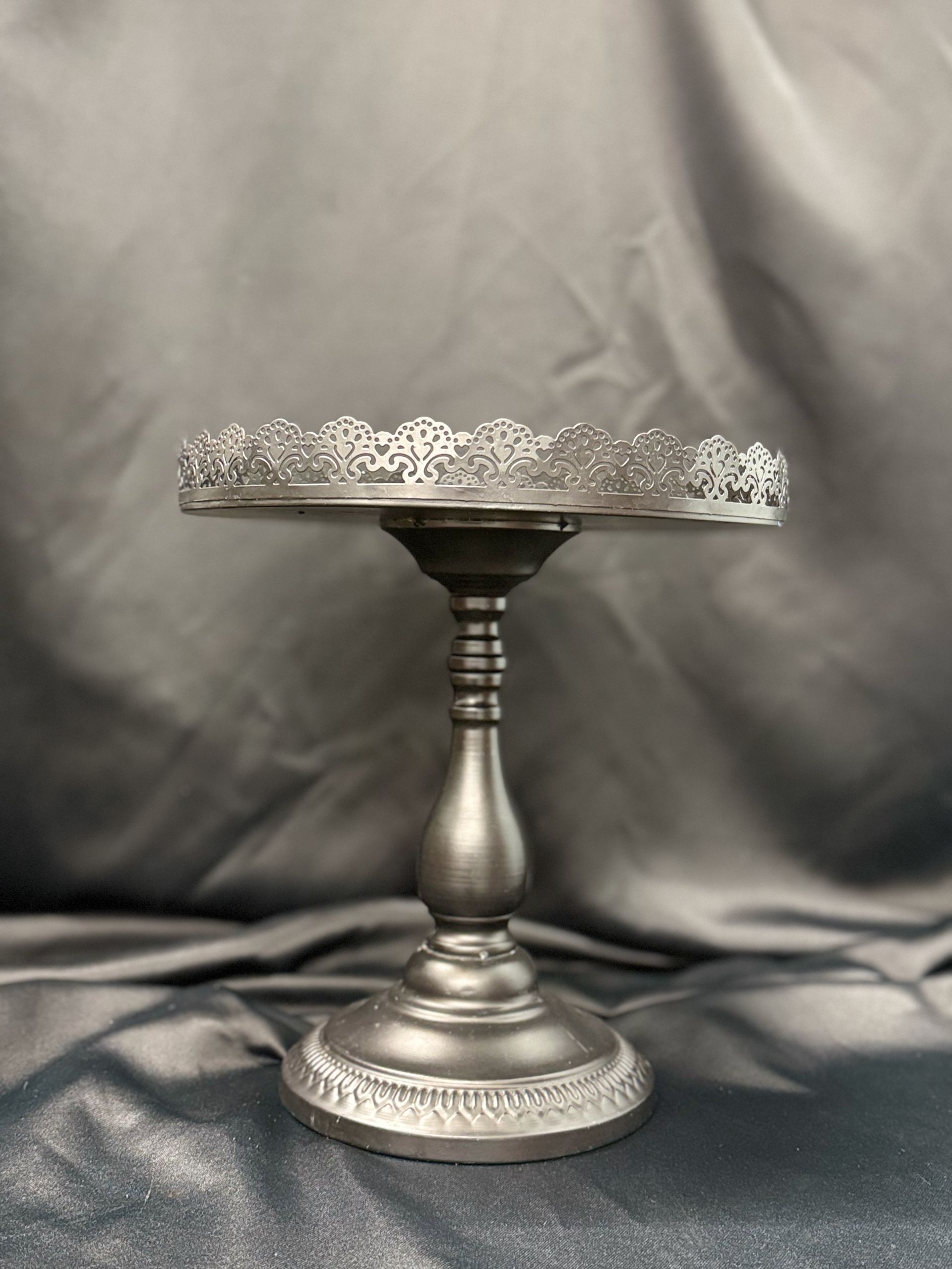 A silver cake stand with a lace top is sitting on a table.