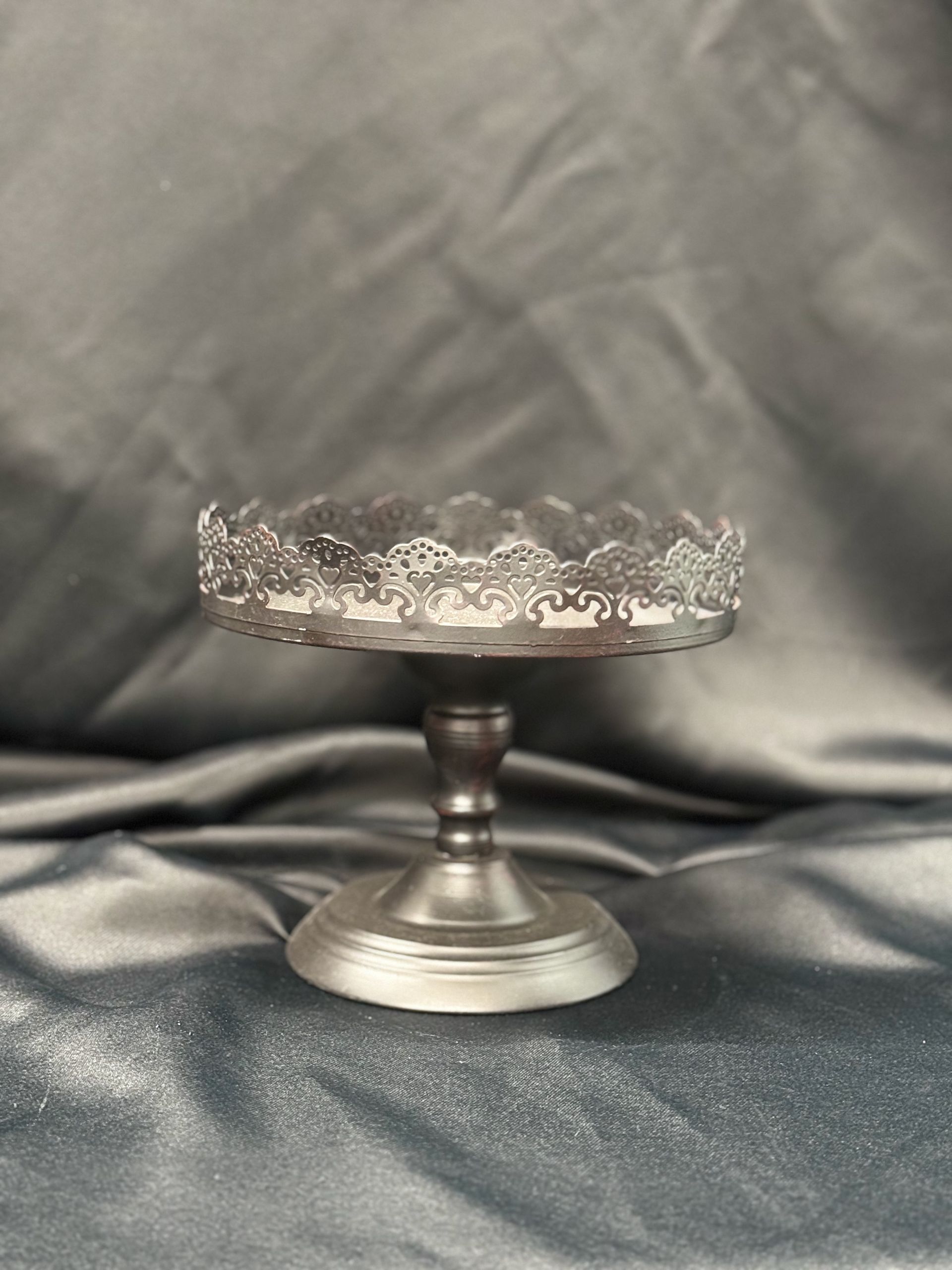 A glass cake stand is sitting on top of a gray cloth.