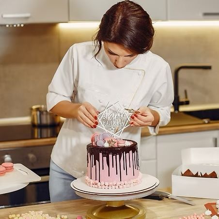 A woman is decorating a cake in a kitchen.
