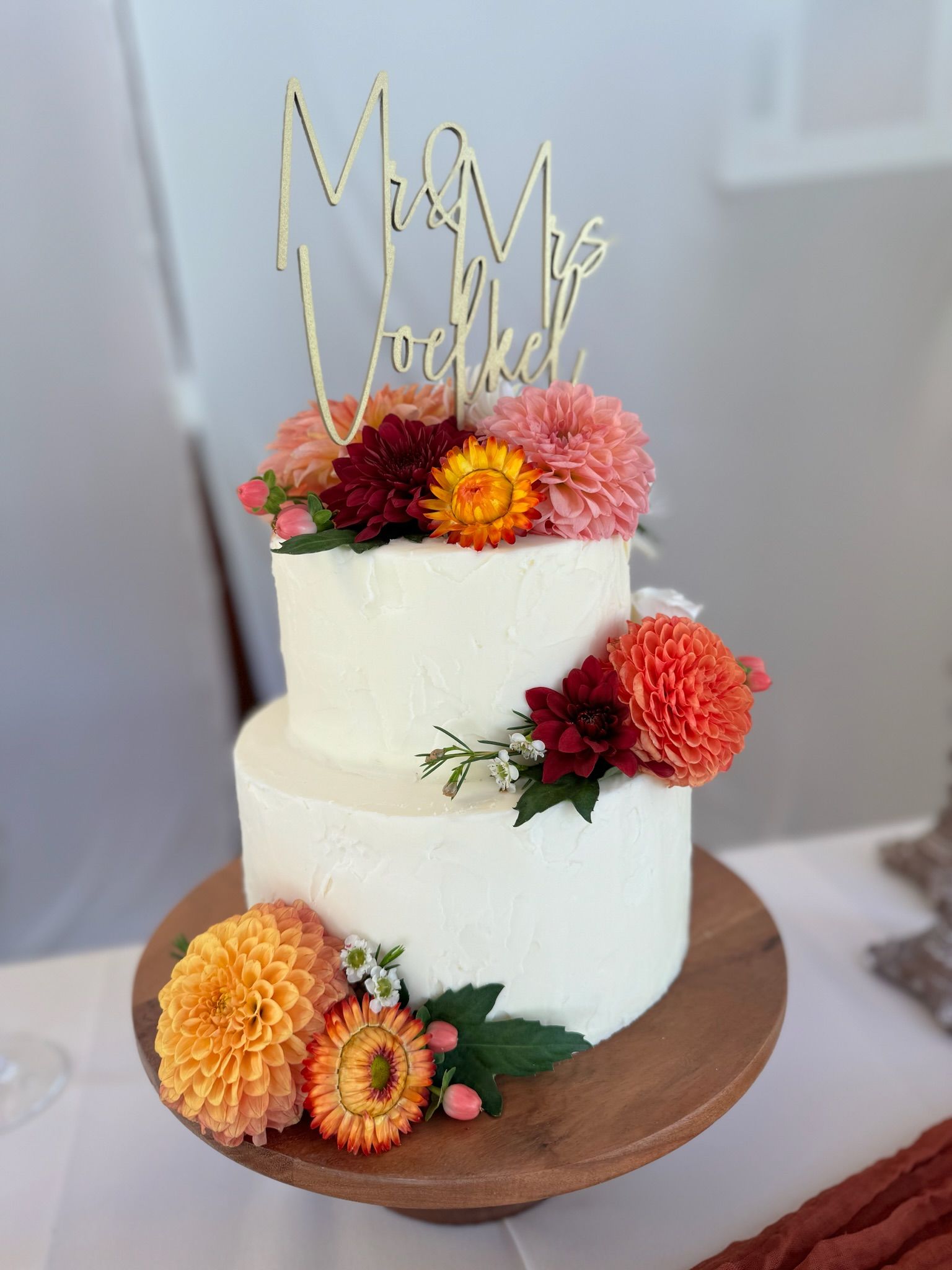 A wedding cake with flowers on top of it on a wooden stand.