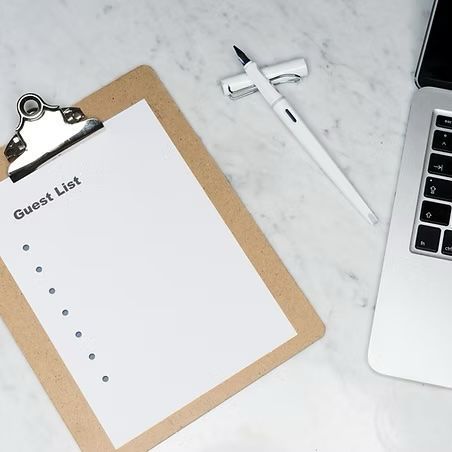 A guest list is on a clipboard next to a laptop