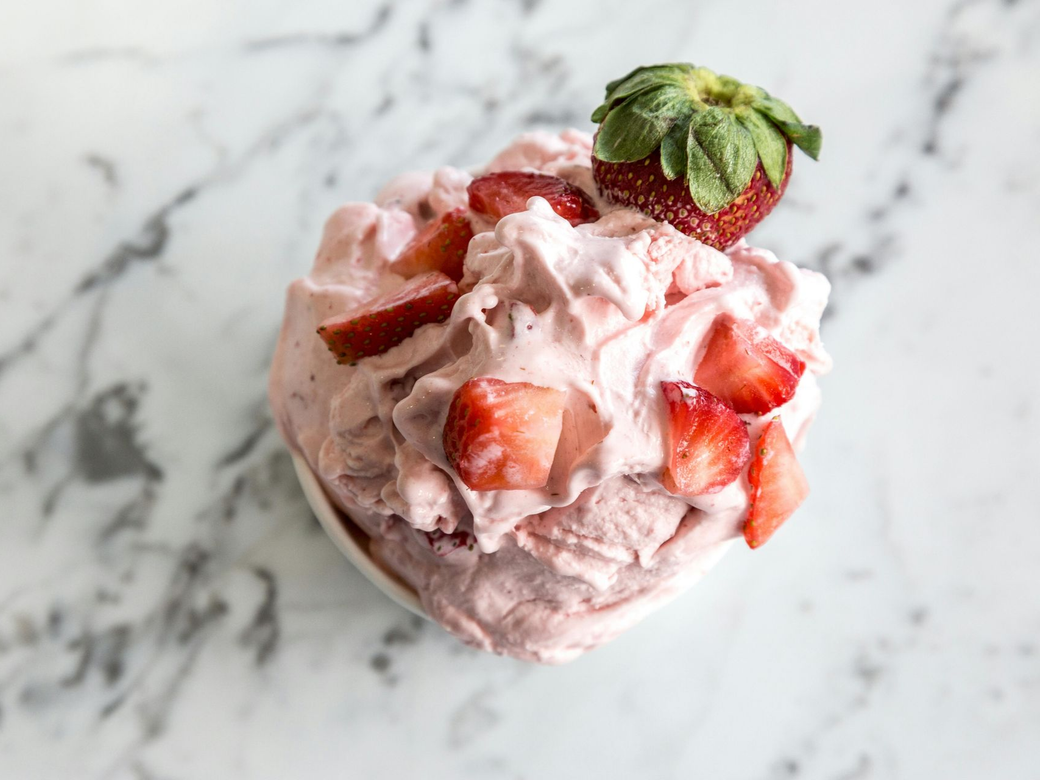 Heart-shaped strawberry dessert topped with fresh strawberry and mint on a marble surface