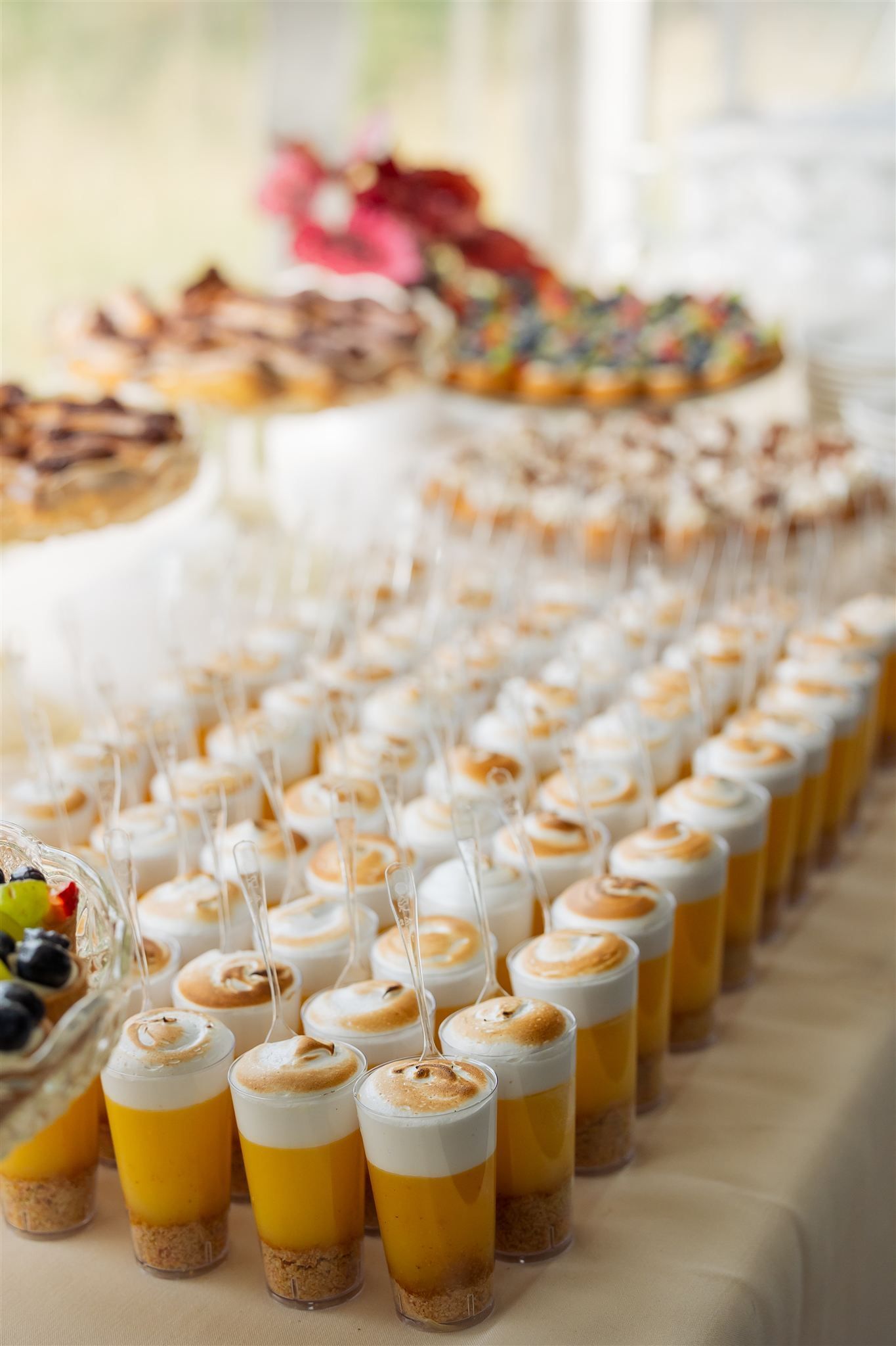 Rows of small dessert cups with white cream and orange layers on a buffet table