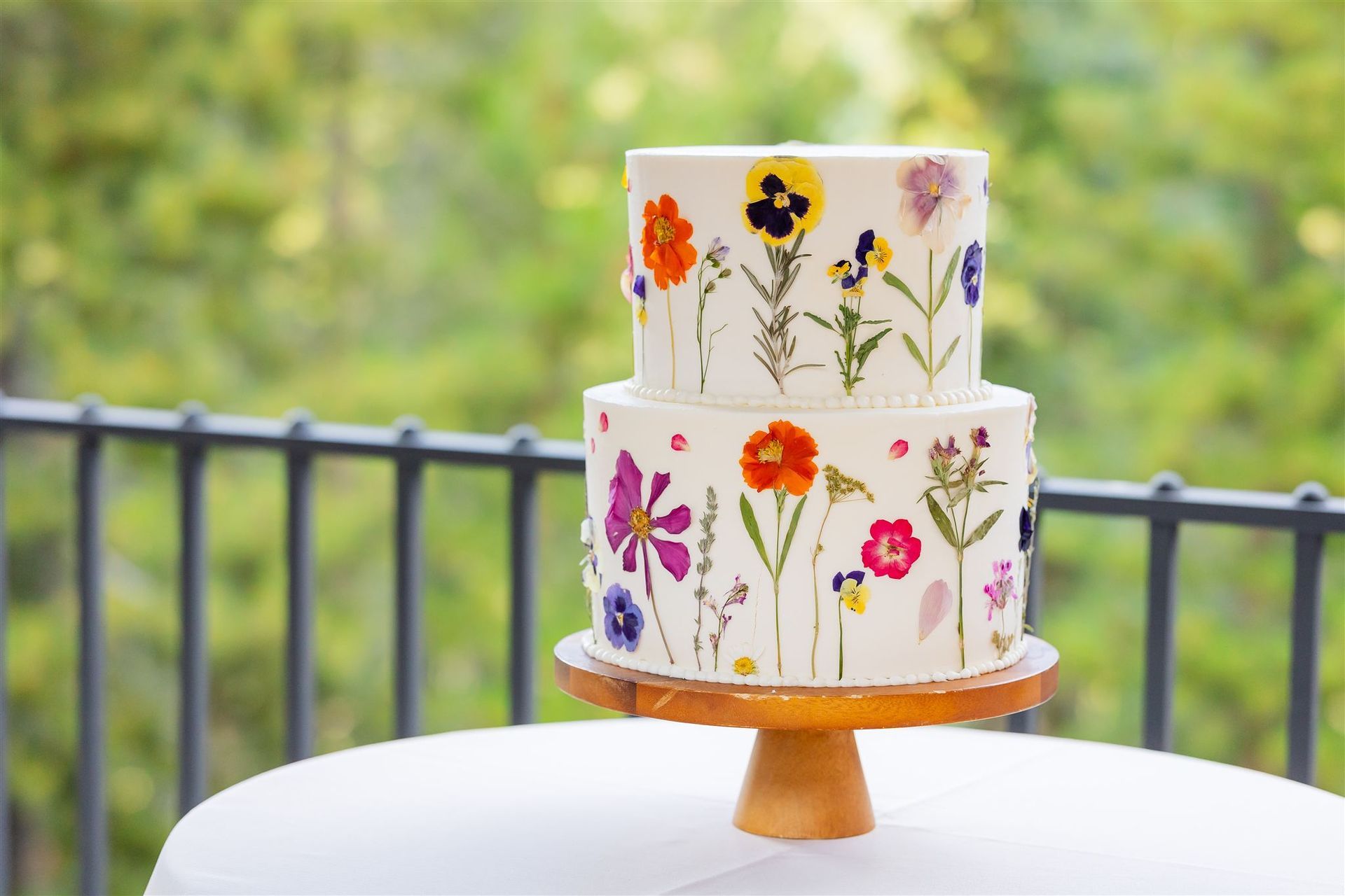 A wedding cake with flowers on top of it is sitting on a table in front of a mountain.