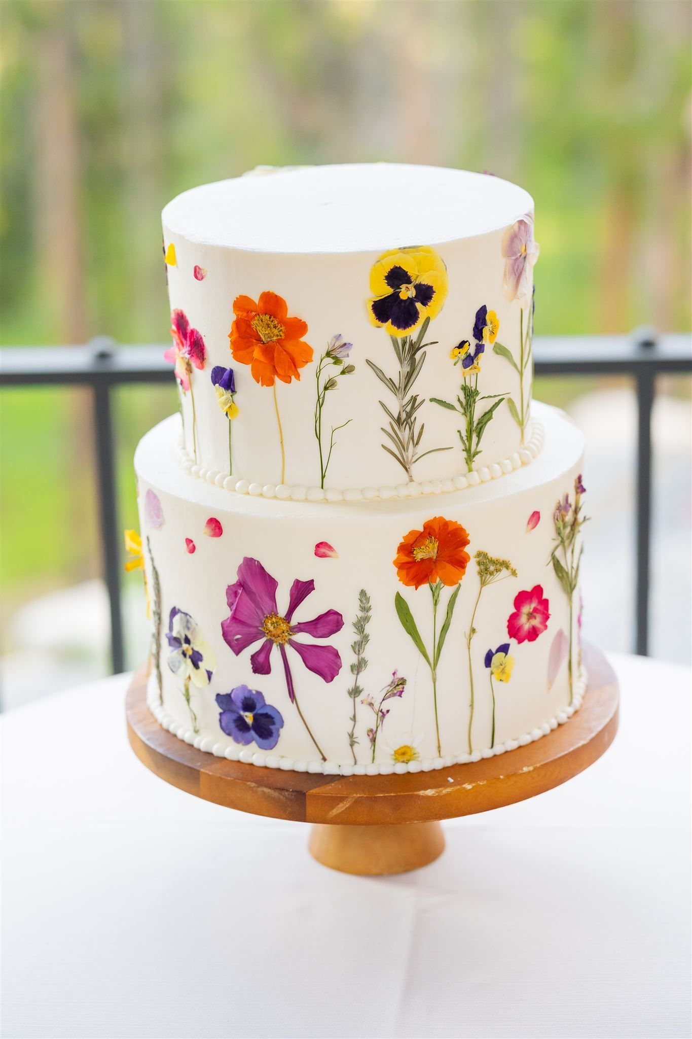 Two-tier white cake with colorful wildflower decorations on a wooden stand