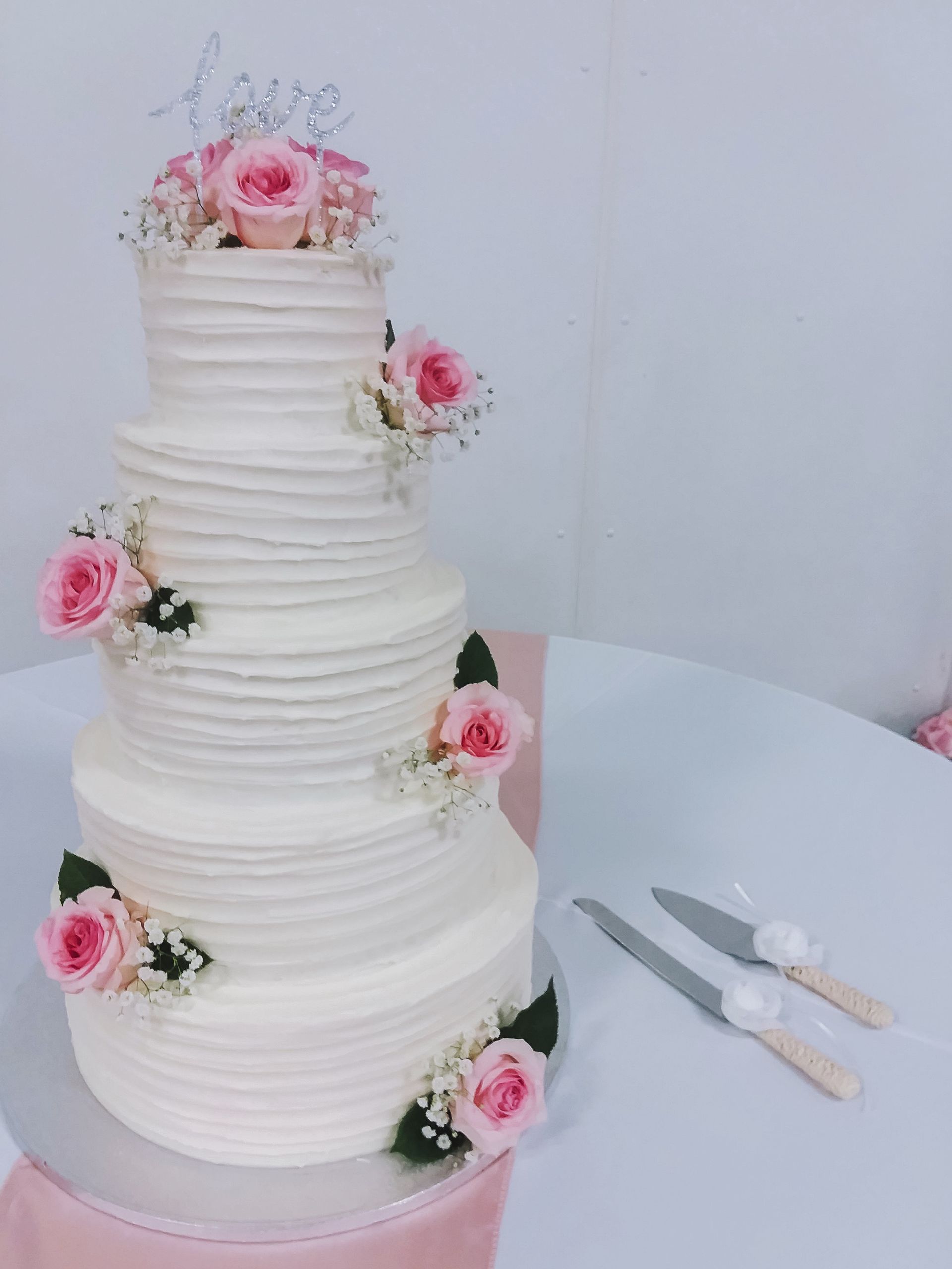 A wedding cake with pink roses and baby 's breath is on a table.