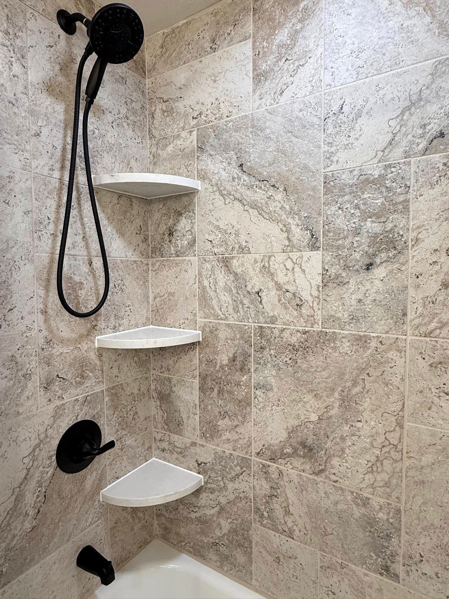 Corner shower with beige tile, black fixtures, and built-in corner shelves.