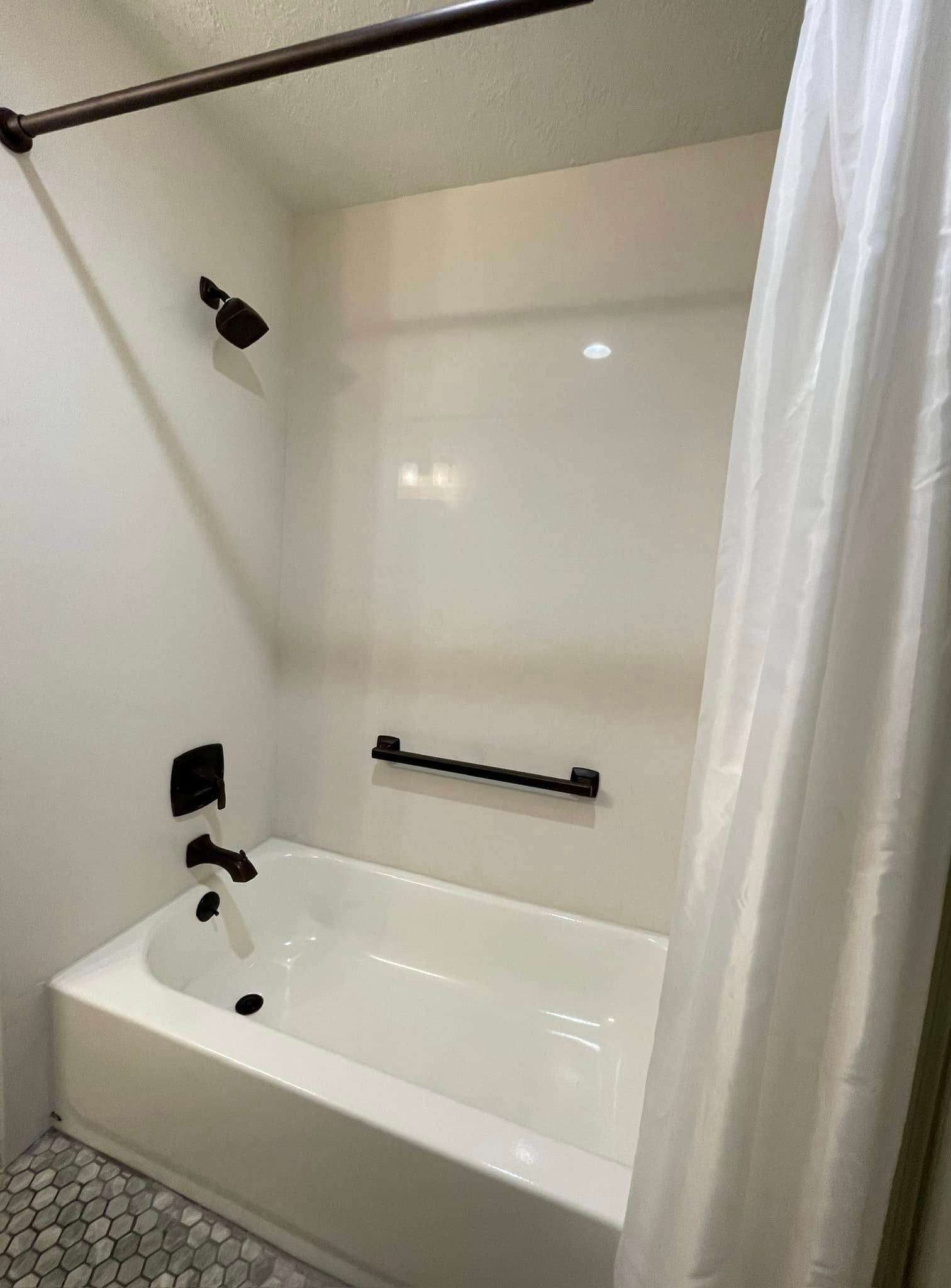 Small white bathroom with a bathtub, black fixtures, and showerhead.
