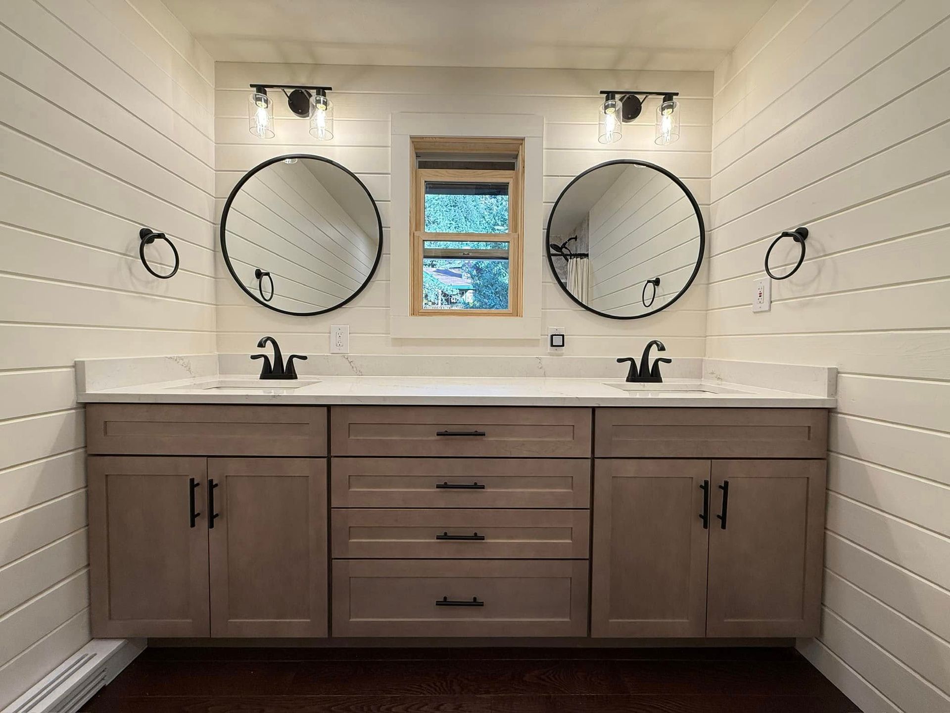 Modern bathroom vanity with double sinks, round mirrors, and a small window above a light wood cabinet
