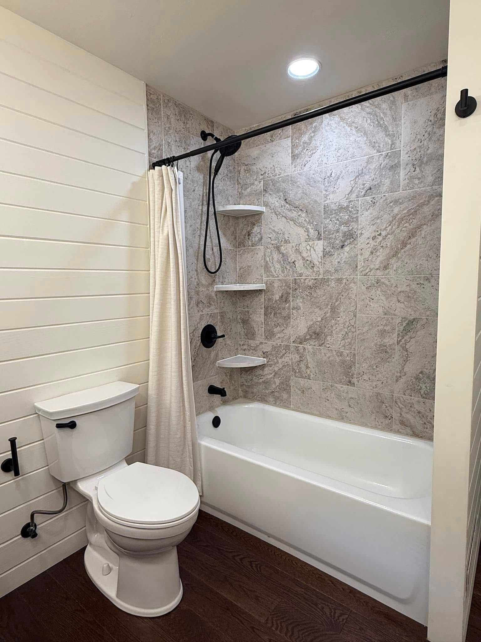 Compact bathroom with white toilet, tub-shower, and gray stone-pattern wall