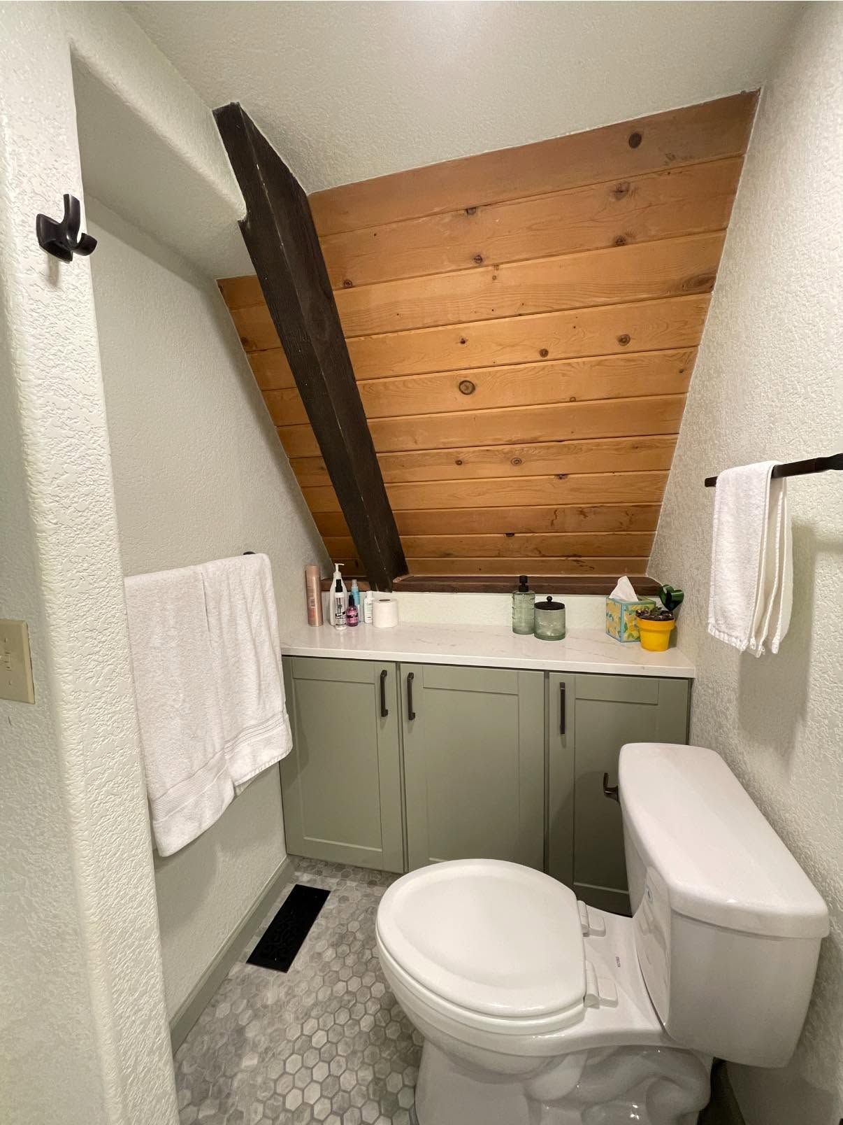 Small bathroom with sloped wood ceiling, gray vanity, toilet, and towel racks.
