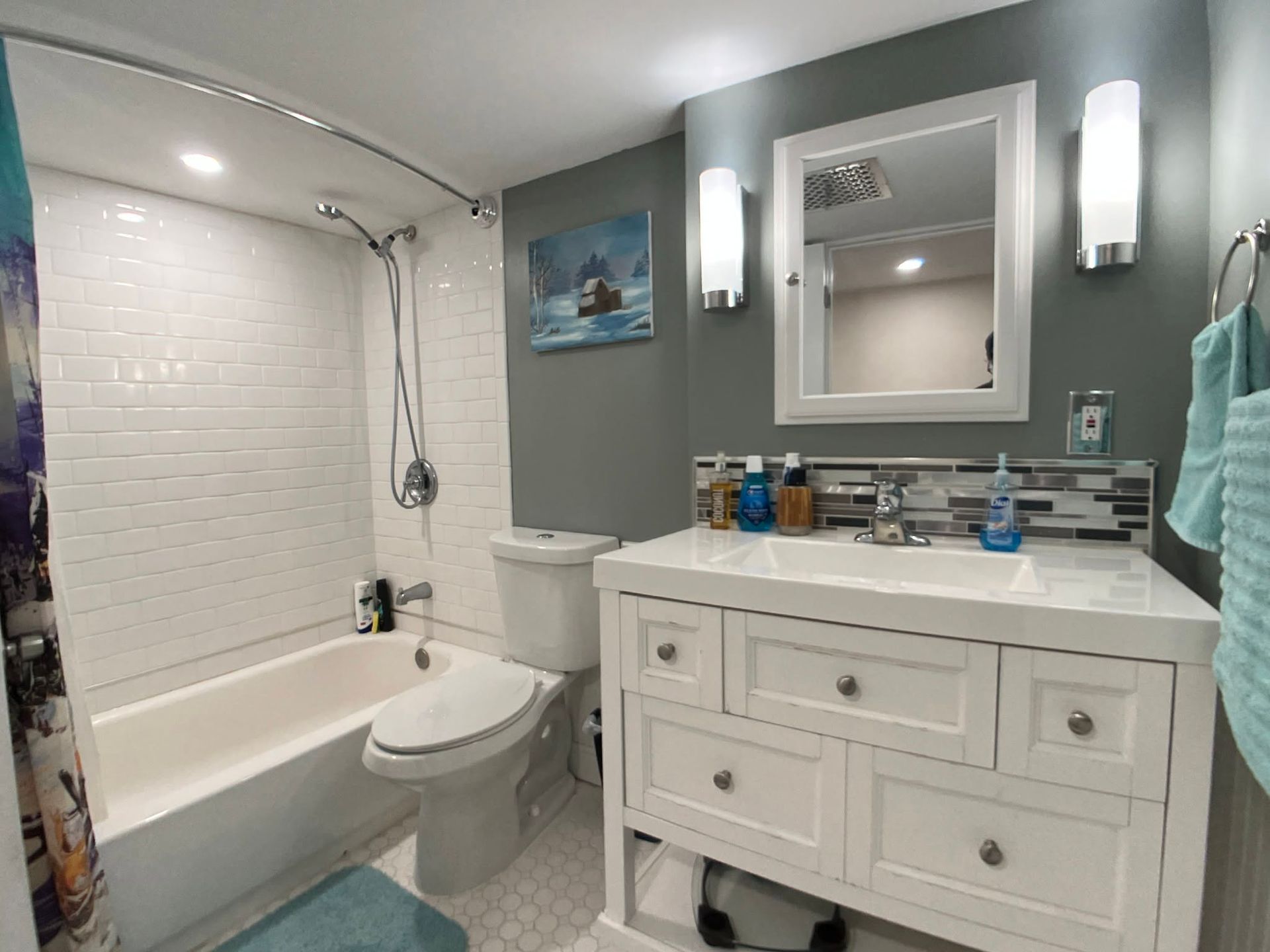 Compact bathroom with white tub, toilet, and vanity against gray walls and tiled shower surround