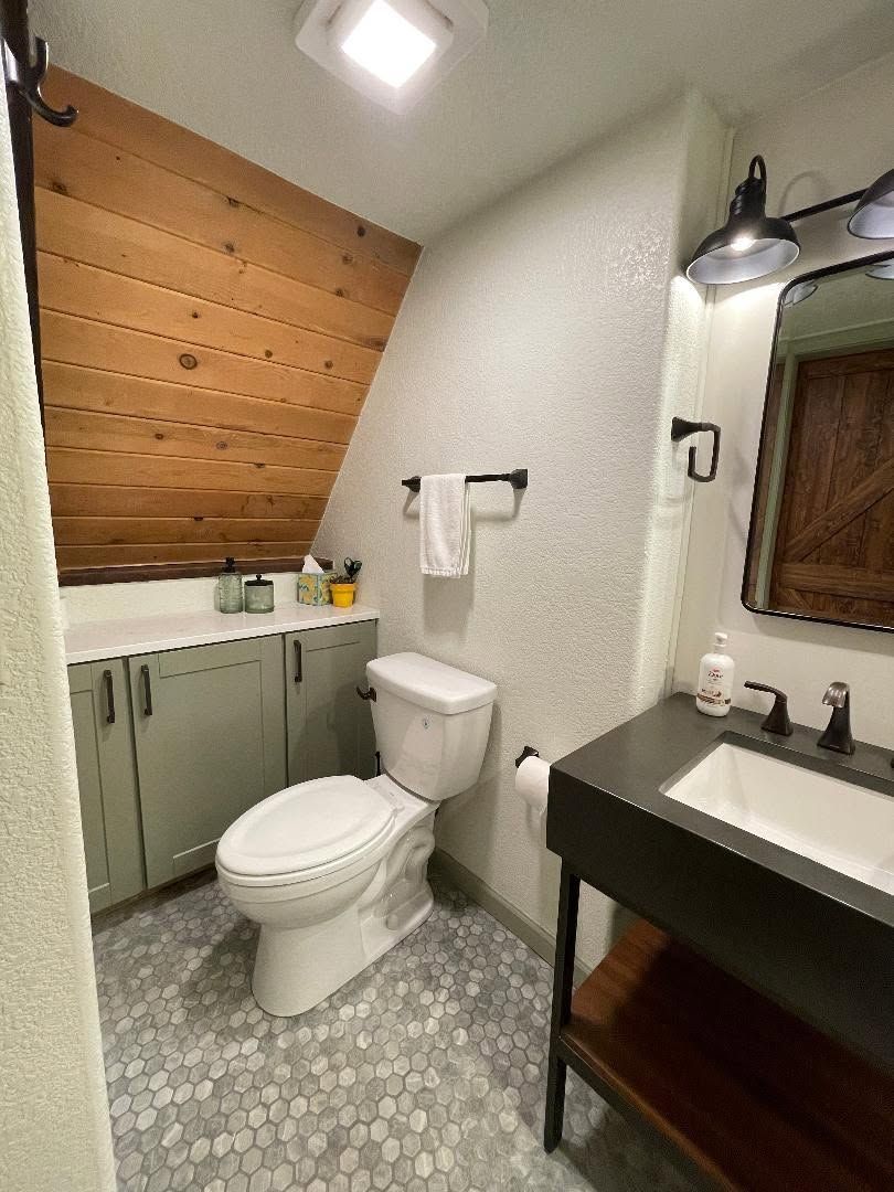 Small bathroom with toilet, vanity, sloped wood ceiling, and gray tile floor.