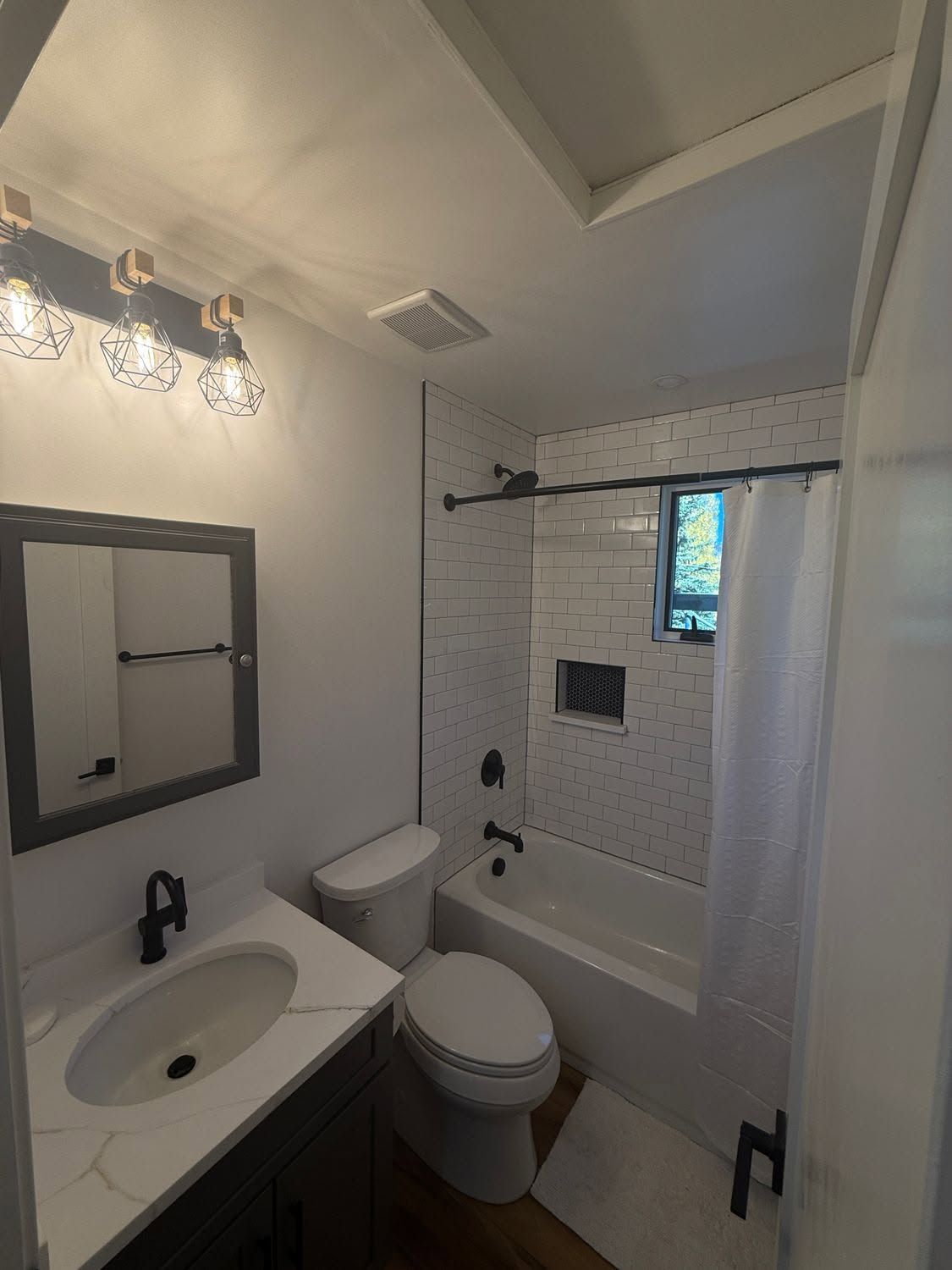 Small bathroom with vanity, toilet, and tiled shower/tub with curtain and window.