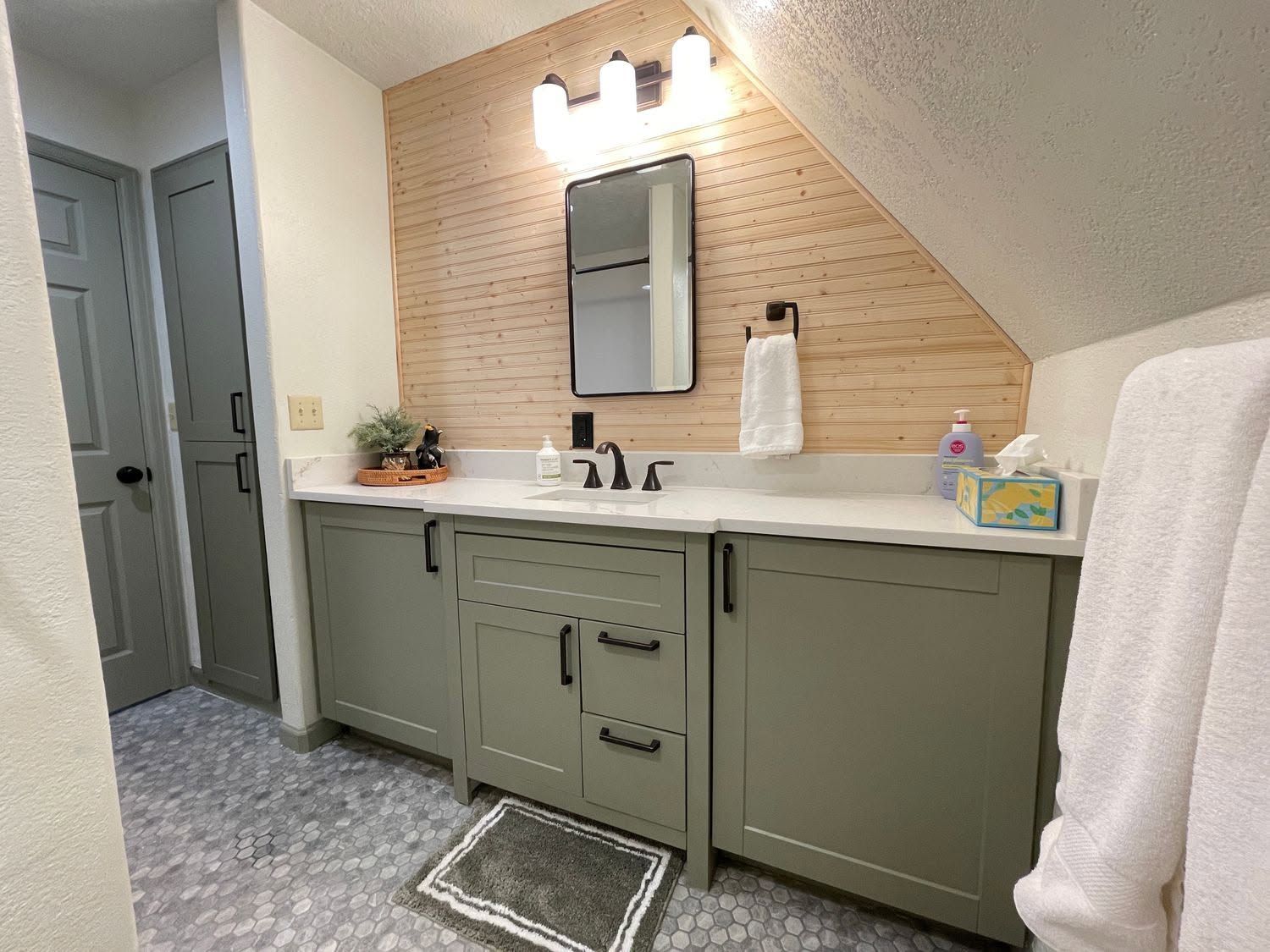 Bathroom vanity with green cabinets, white countertop, mirror, and towel under warm lights