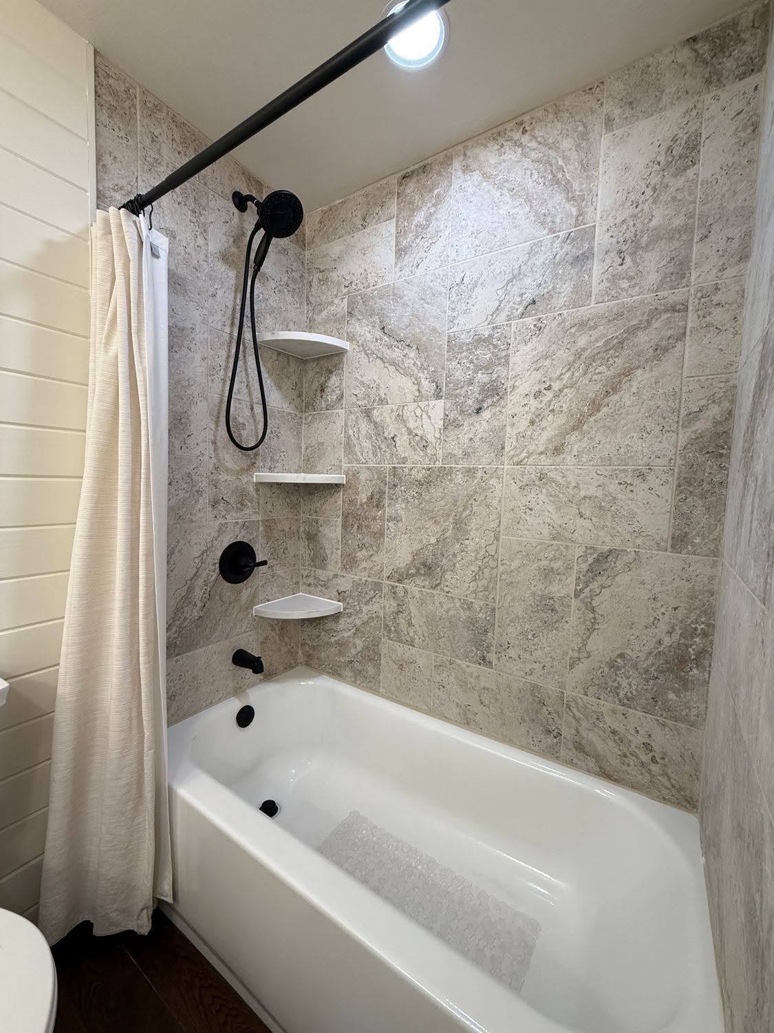 Accessible shower-tub combo with grab bars, shower curtain, and marble-look wall tiles