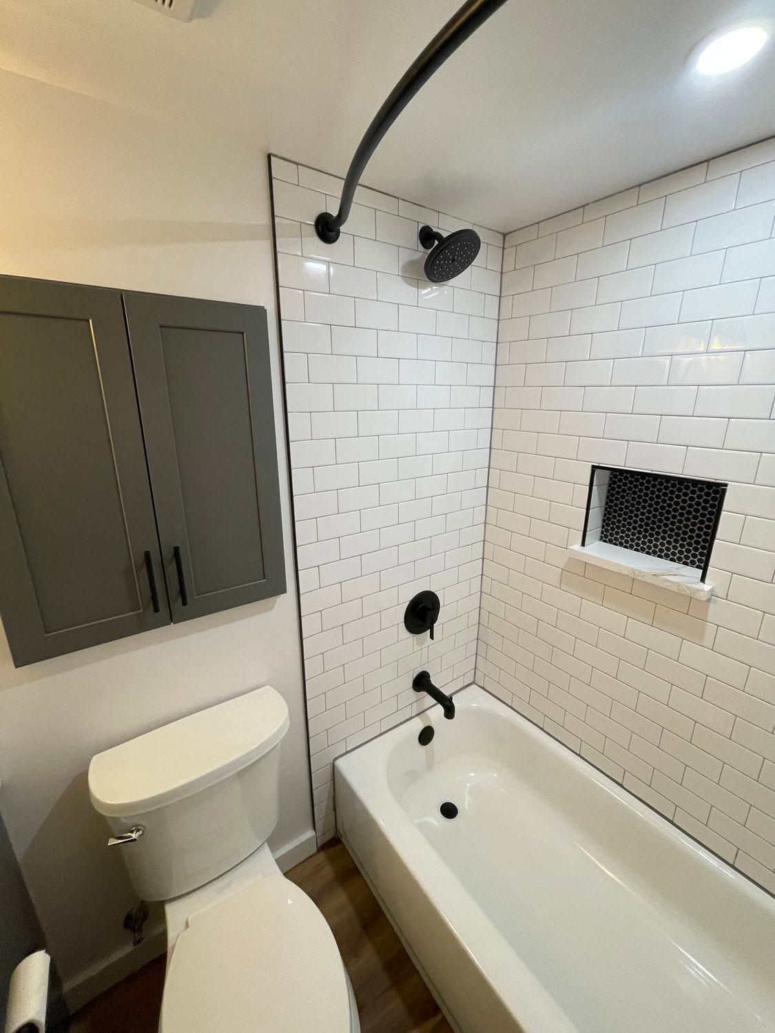 Small bathroom with white subway tile, tub, toilet, dark cabinets, and a showerhead over the tub.