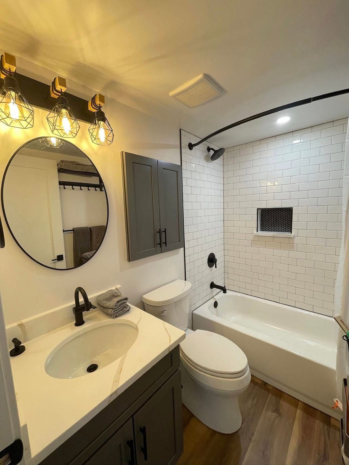Small bathroom with vanity, round mirror lights, toilet, and tub with white tile shower surround.