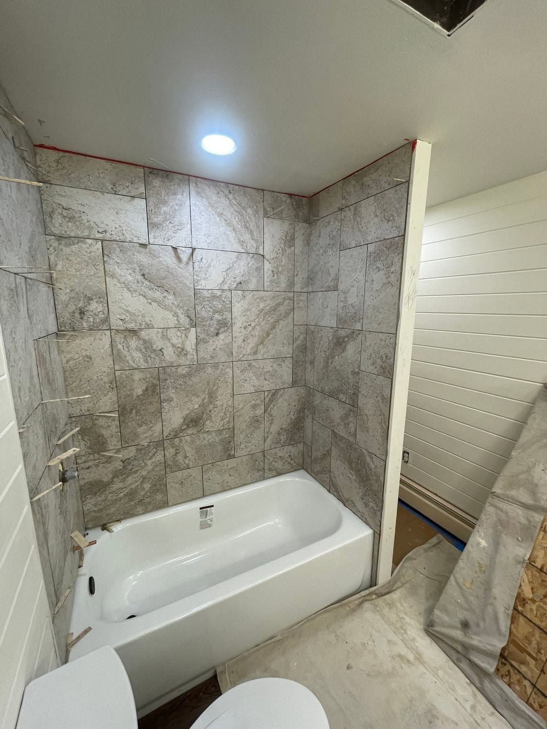 Small marble-tiled bathroom with a white bathtub and bright ceiling light.