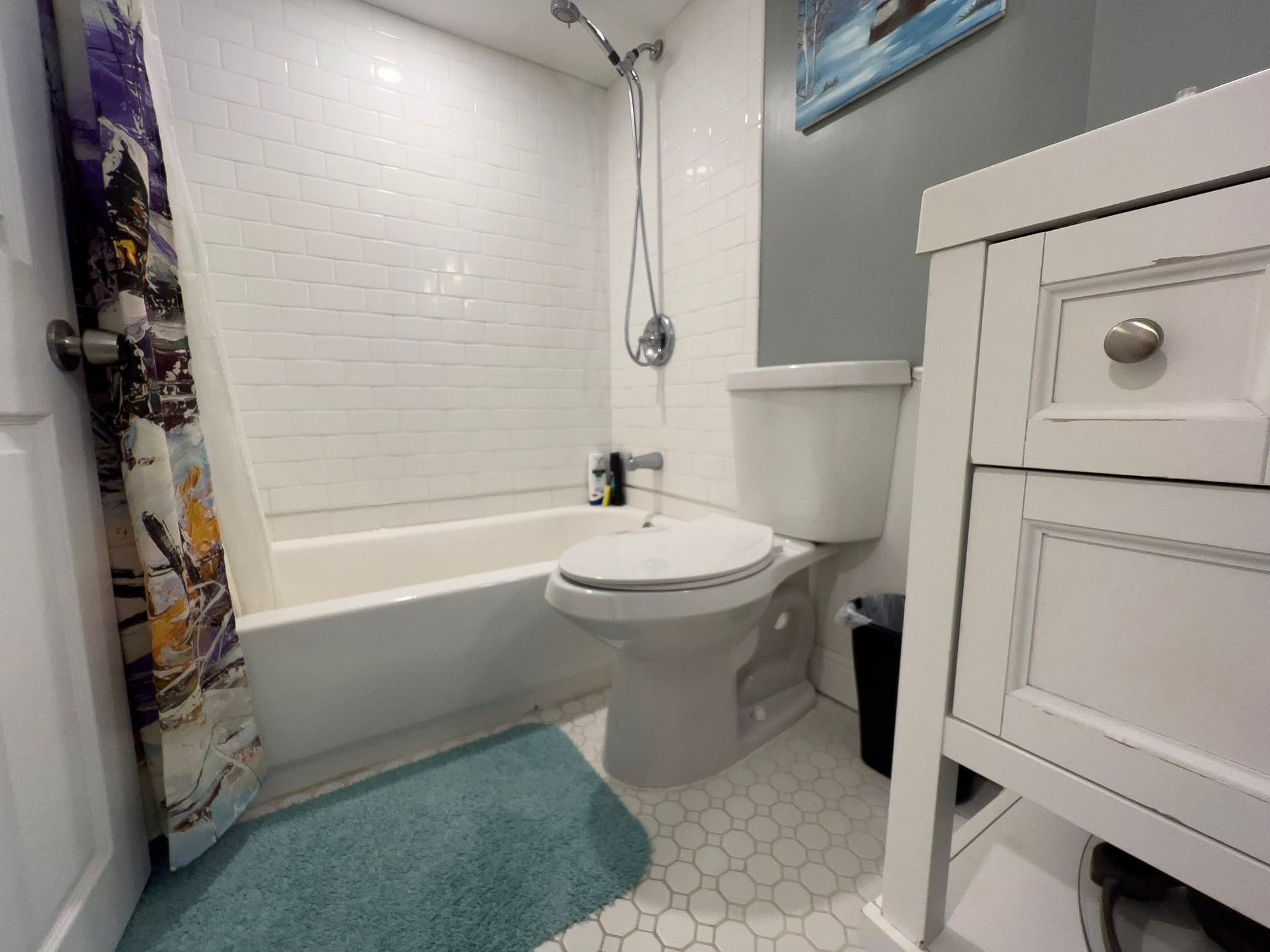 Small bathroom with white tub, toilet, sink vanity, gray walls, and teal rug.