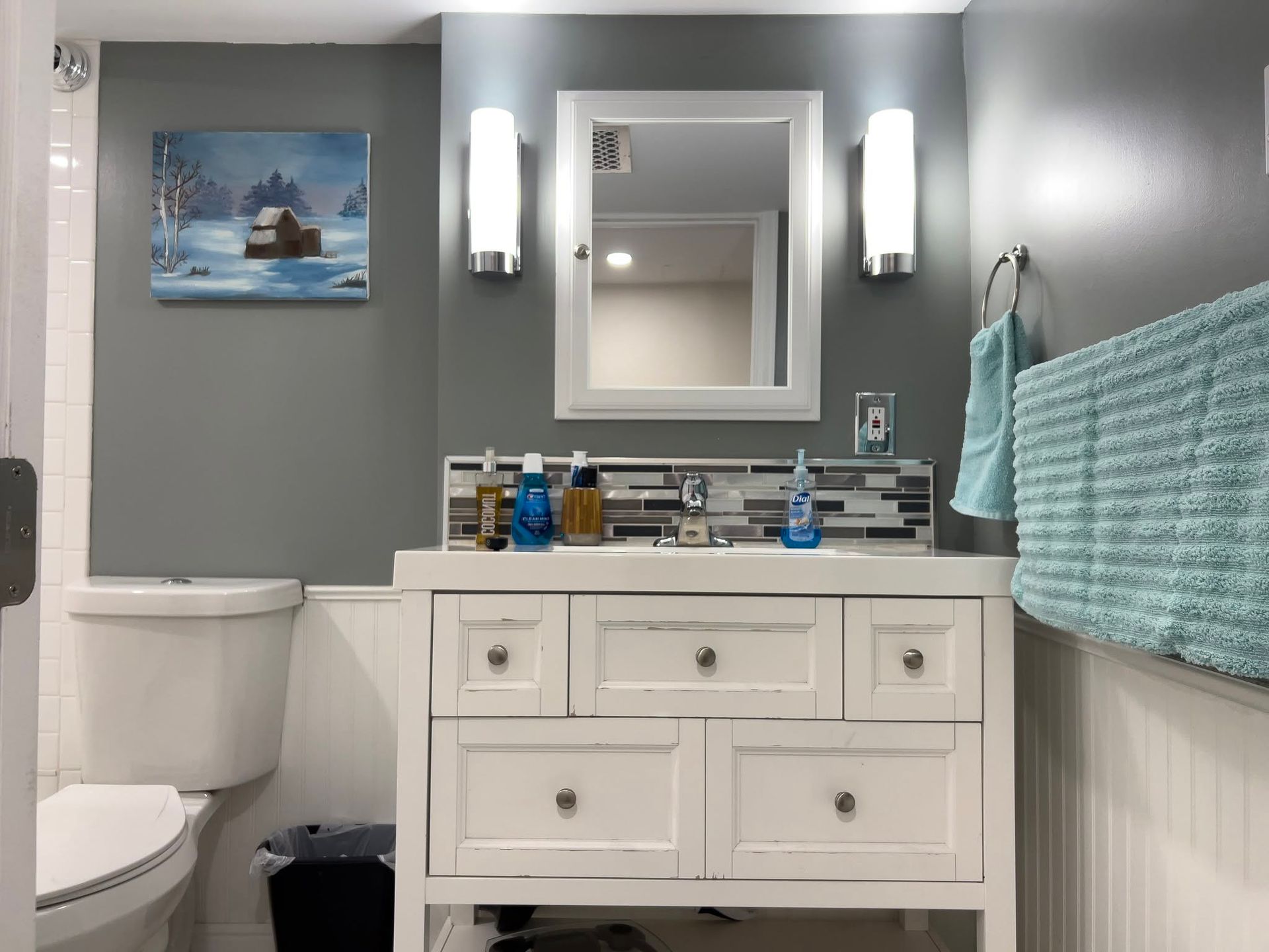Modern gray bathroom with white vanity, mirror, sconces, toilet, and teal towel accents.
