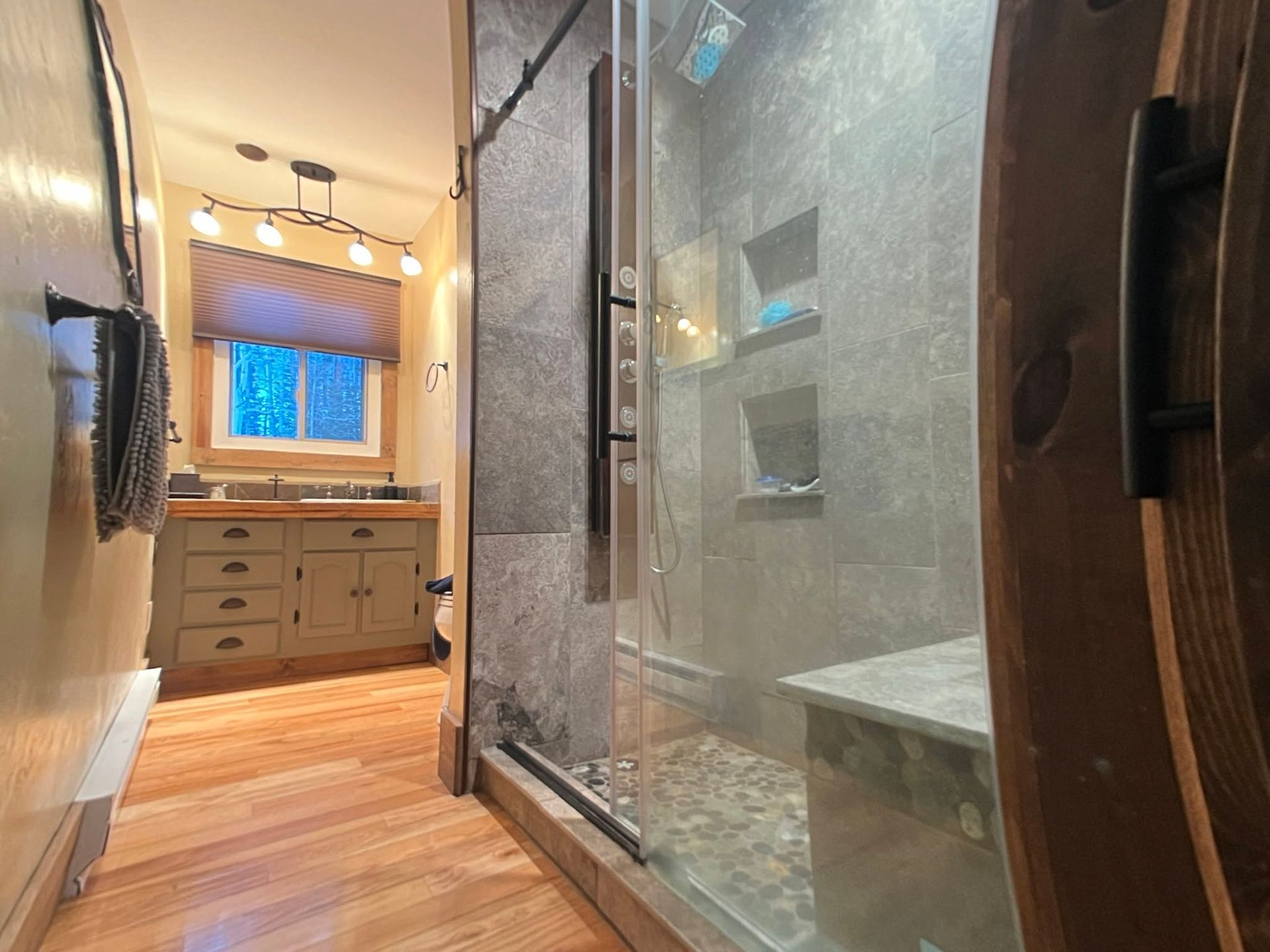 Modern bathroom with glass shower, wood vanity, and warm string lights by a window