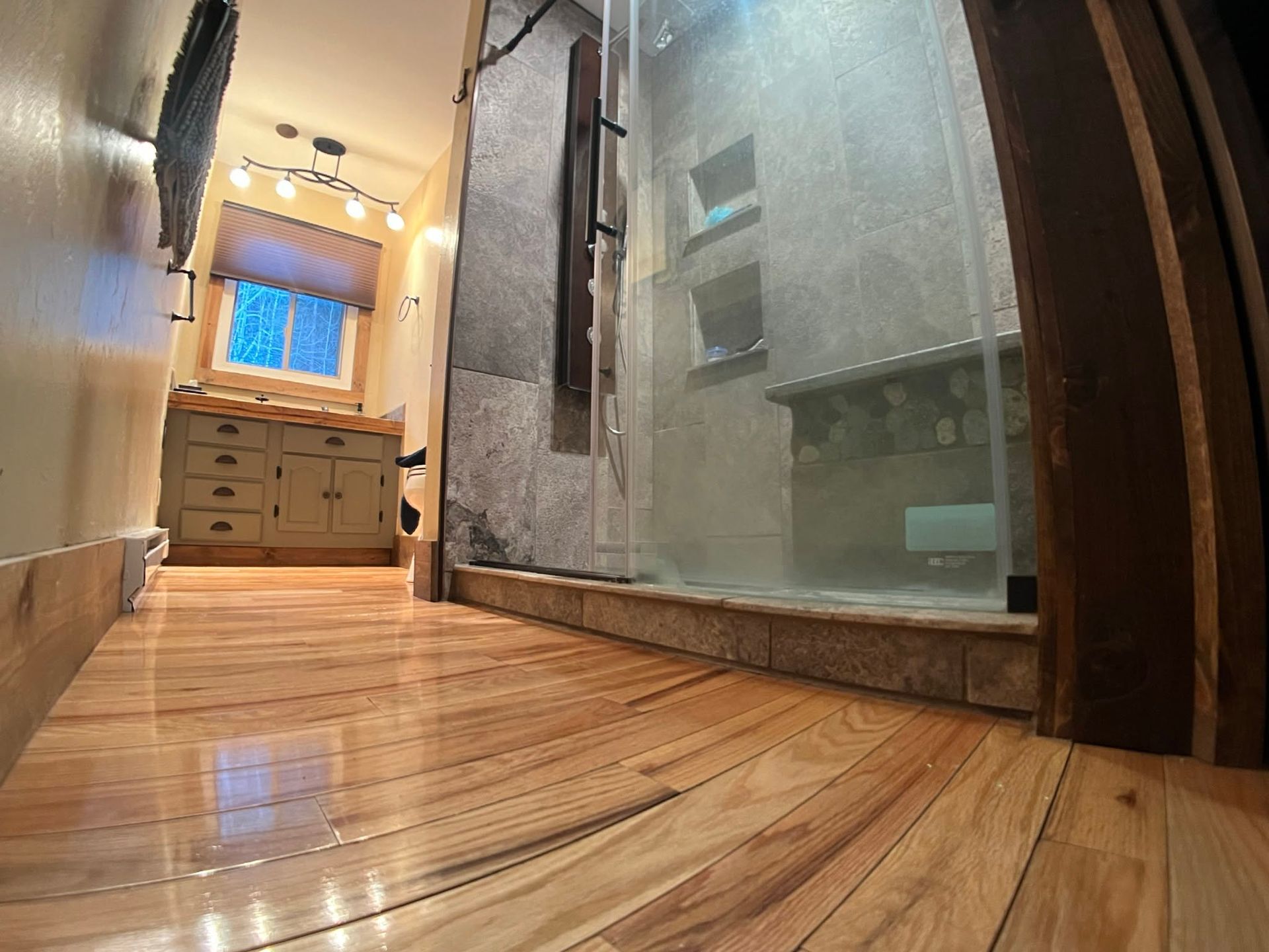 Narrow bathroom hallway with wood floor, vanity at end, and frosted shower glass on the right.