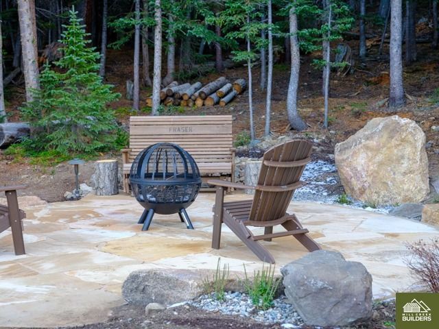 Outdoor fire pit area with two wooden chairs on a stone patio beside rocks and trees