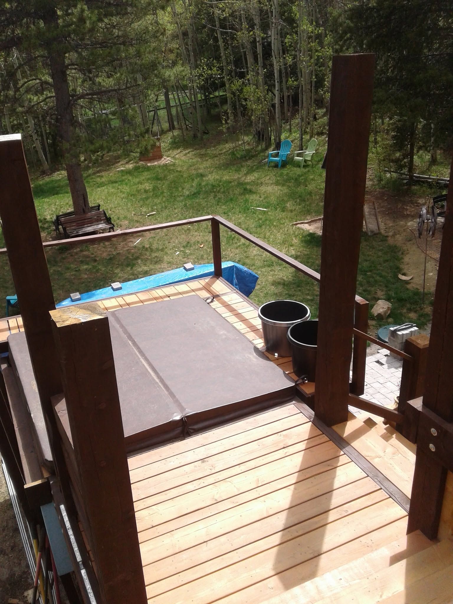 Wooden deck steps and railing overlooking a grassy wooded backyard with a blue tarp and chairs.