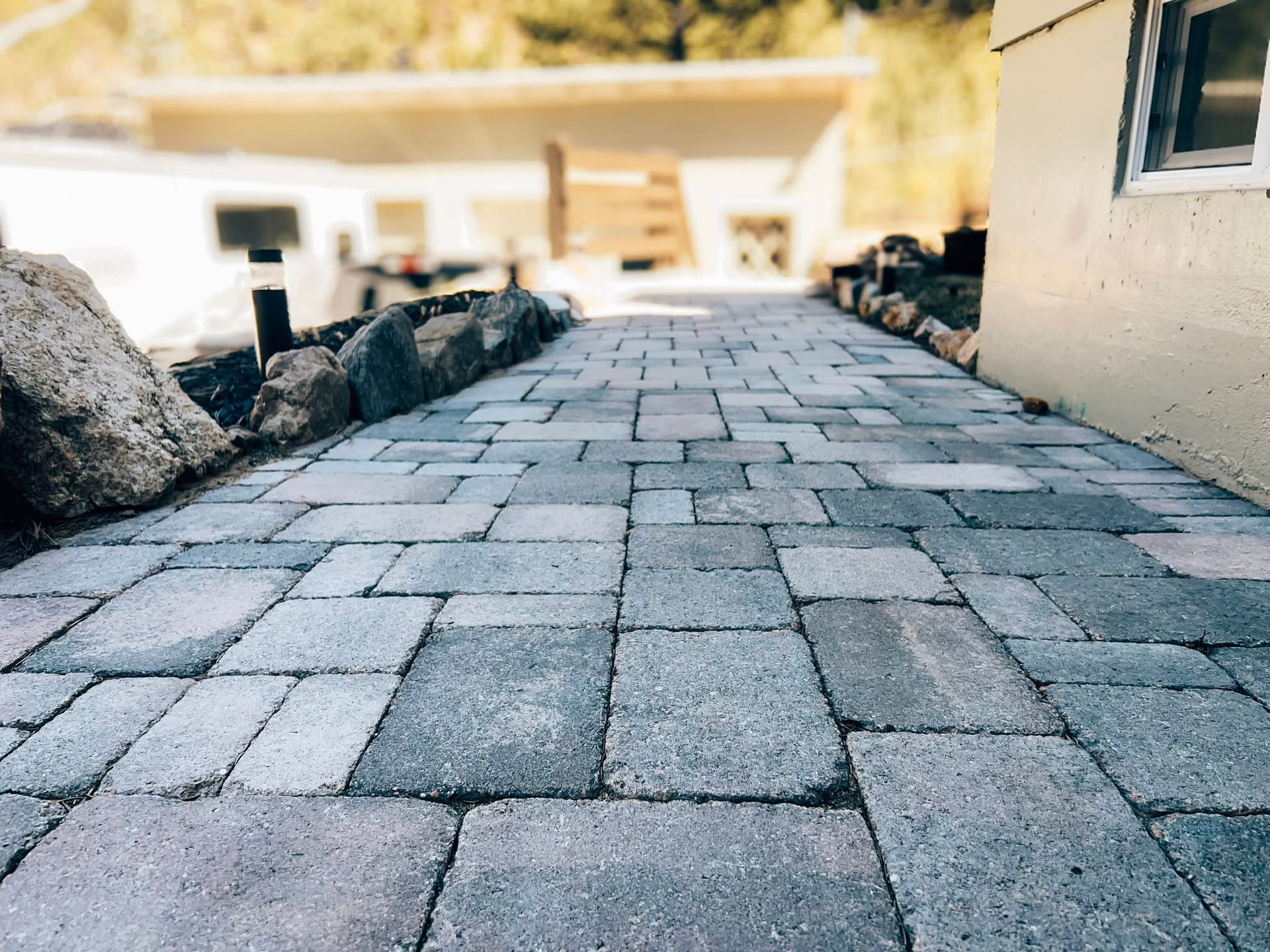 Stone-paved walkway leading toward a bright building entrance, lined with rocks on both sides