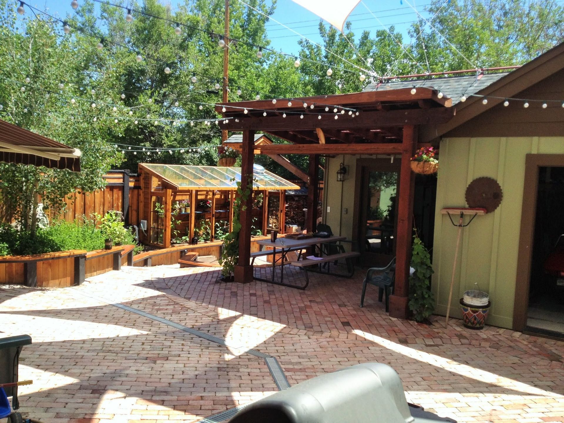 Outdoor patio with tables, pergola, potted plants, and brick paving beside a building