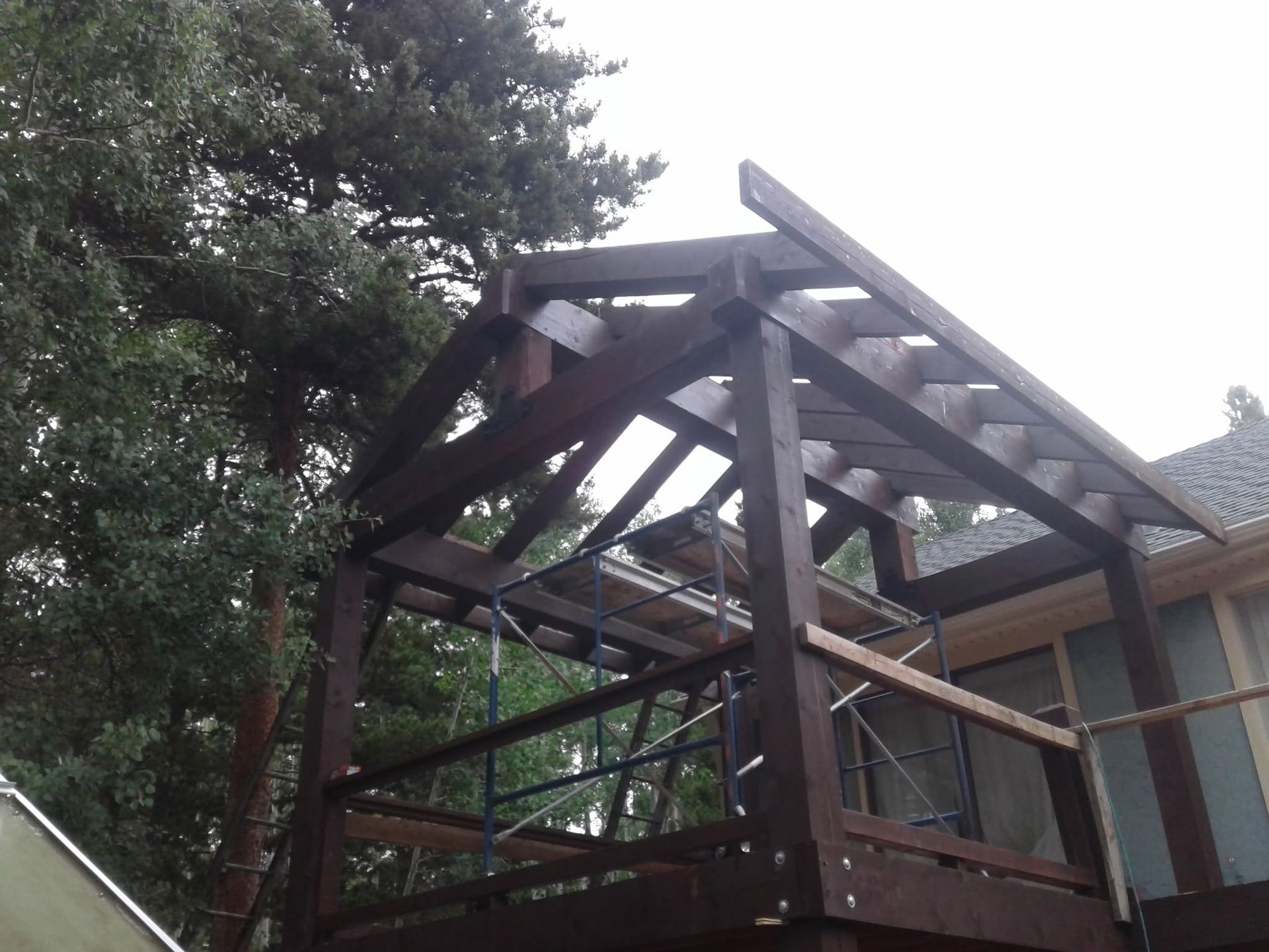 Collapsed wooden deck roof beside a house, with exposed beams and trees in the background