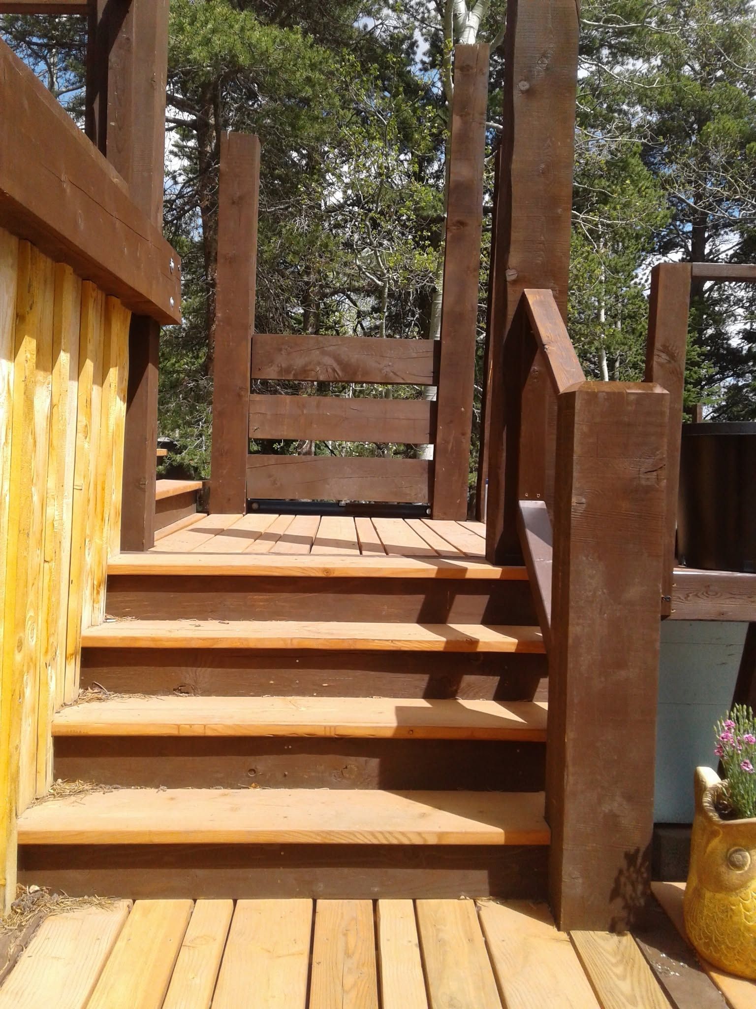 Wooden outdoor staircase leading to a small deck with railings and trees in the background